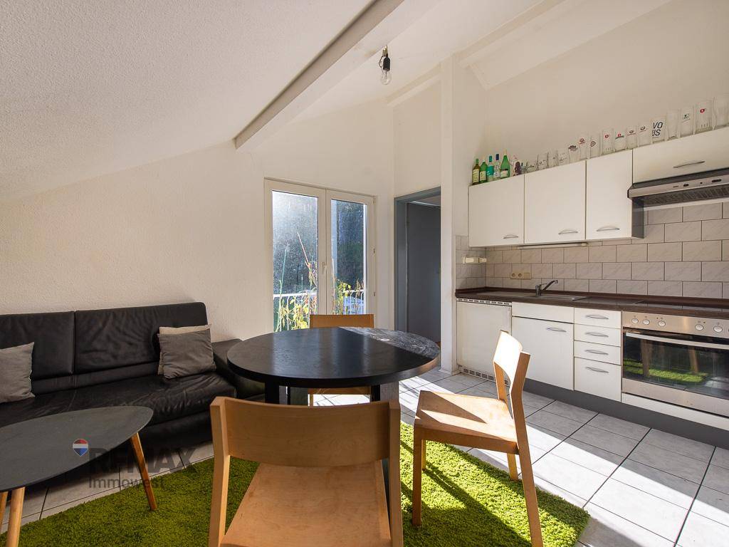 Heller Wohnbereich im Dachgeschoss mit integrierter Küche und Zugang zu einem kleinen Balkon.