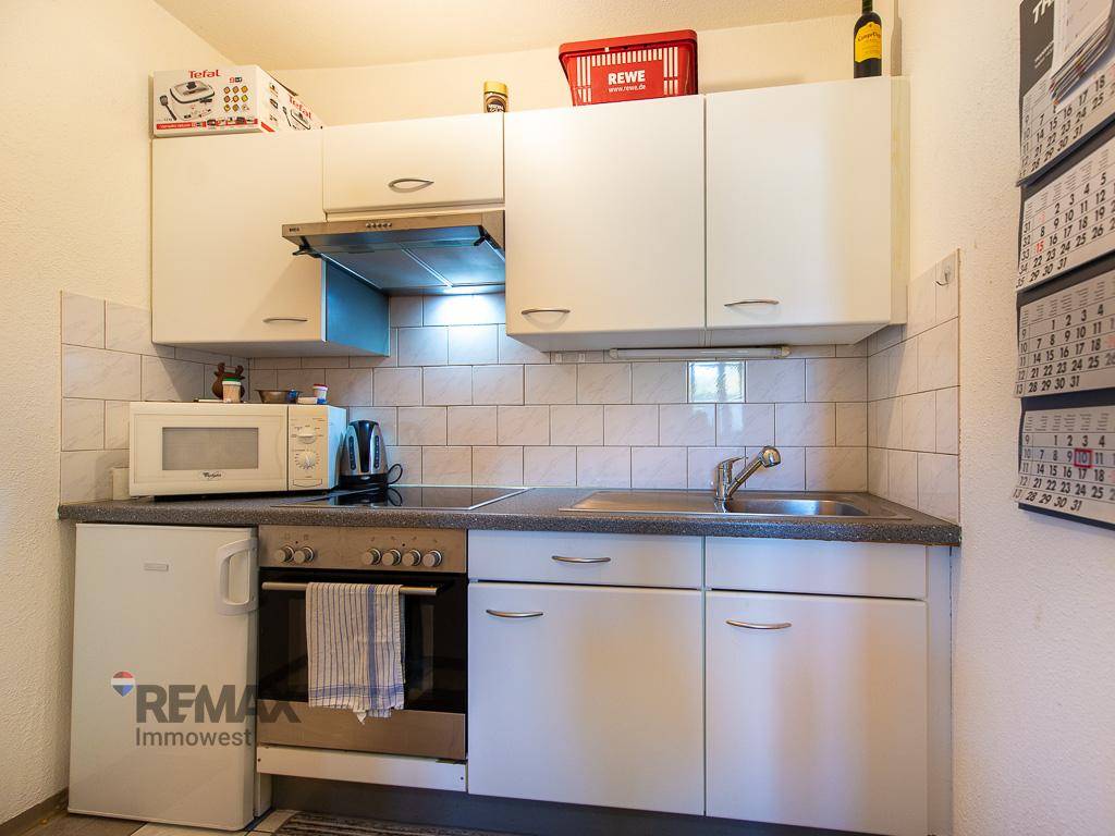 Kleine Küchenzeile mit weißen Schränken, Mikrowelle, Backofen und Kühlschrank, effizient eingerichtet.