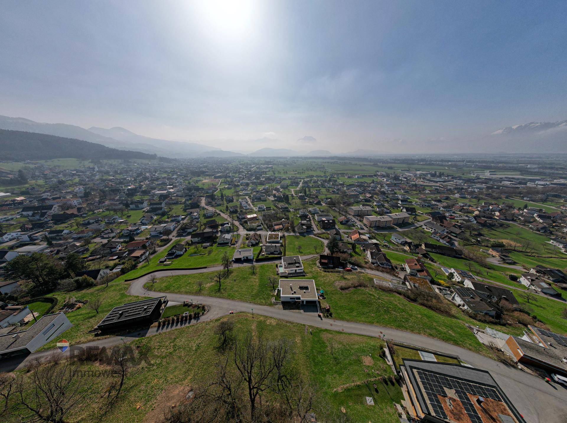 Weitläufige Panorama-Luftaufnahme einer Stadt im Tal, umgeben von Bergen unter hellem Himmel.