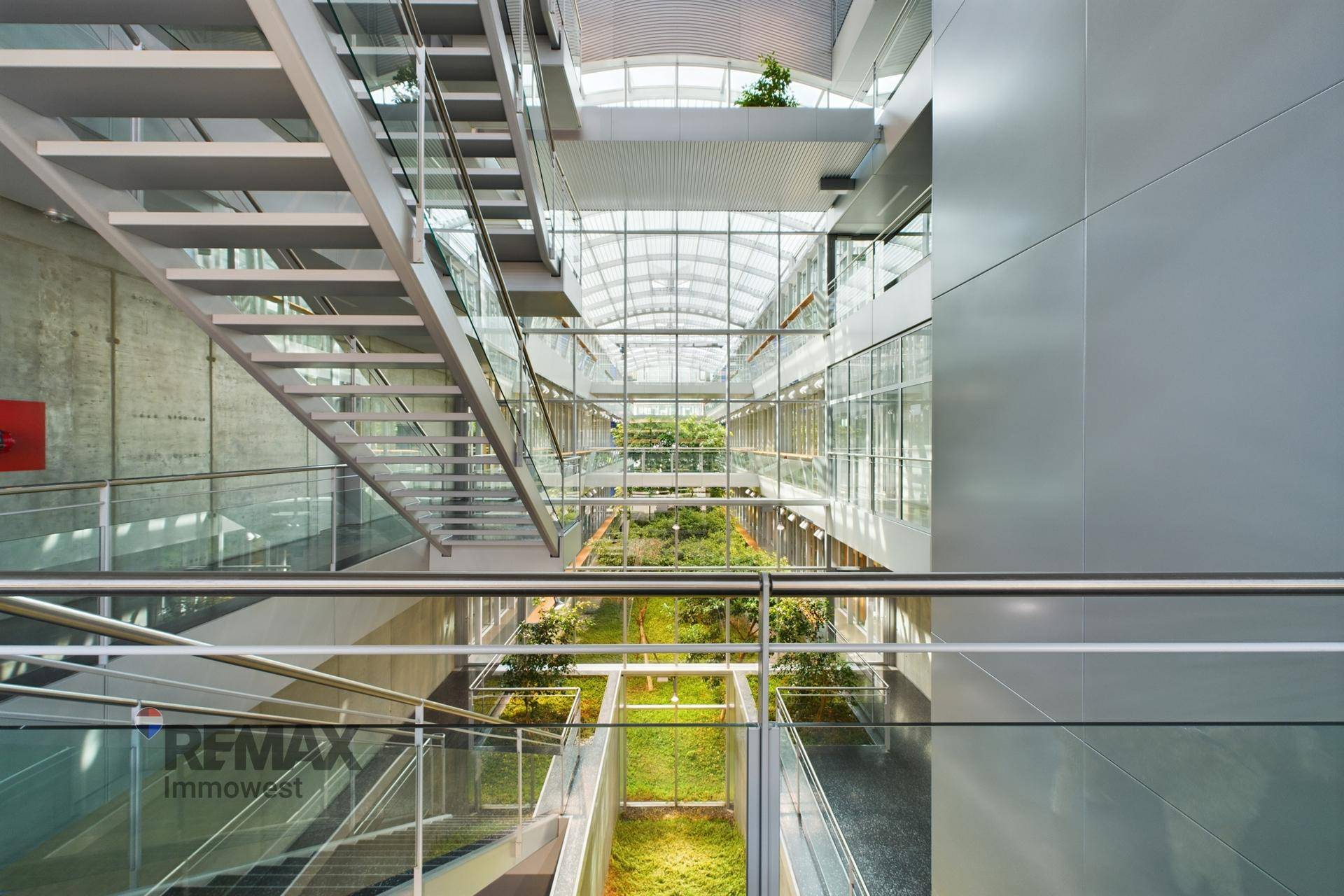 Beeindruckendes Atrium mit Glasdach, modernen Treppen und üppiger Innenbegrünung.