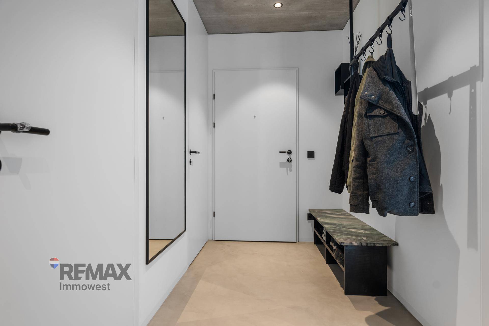 Heller Eingangsbereich mit Garderobe, großem Spiegel und moderner, schlichter Gestaltung.