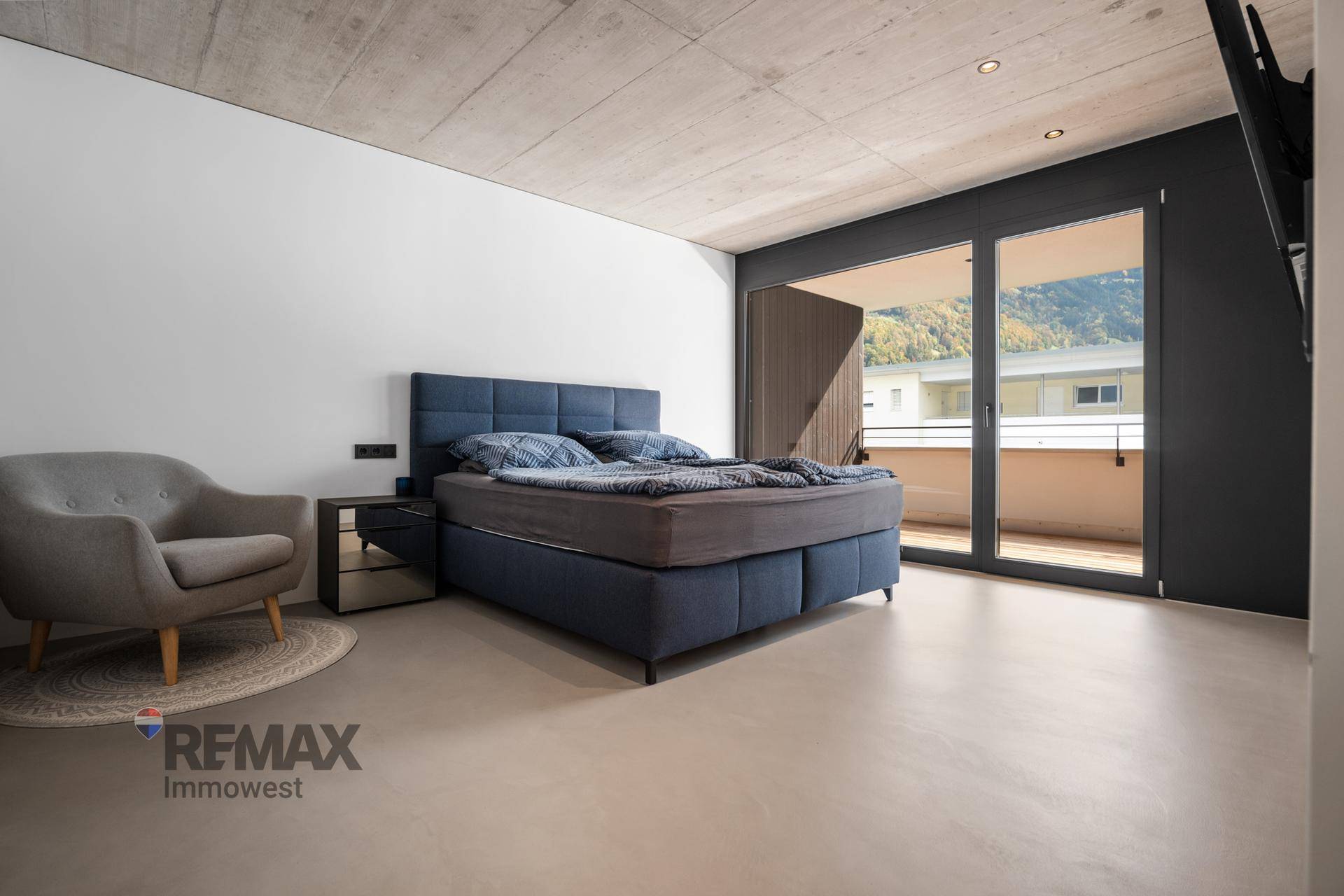 Schlafzimmer mit modernem Boxspringbett, minimalistischer Einrichtung und Zugang zu einem Balkon.