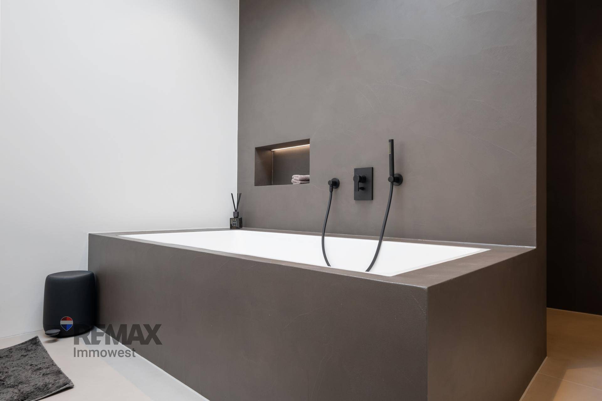 Elegantes Badezimmer mit integrierter Badewanne und modernen schwarzen Armaturen in minimalistischem Design.