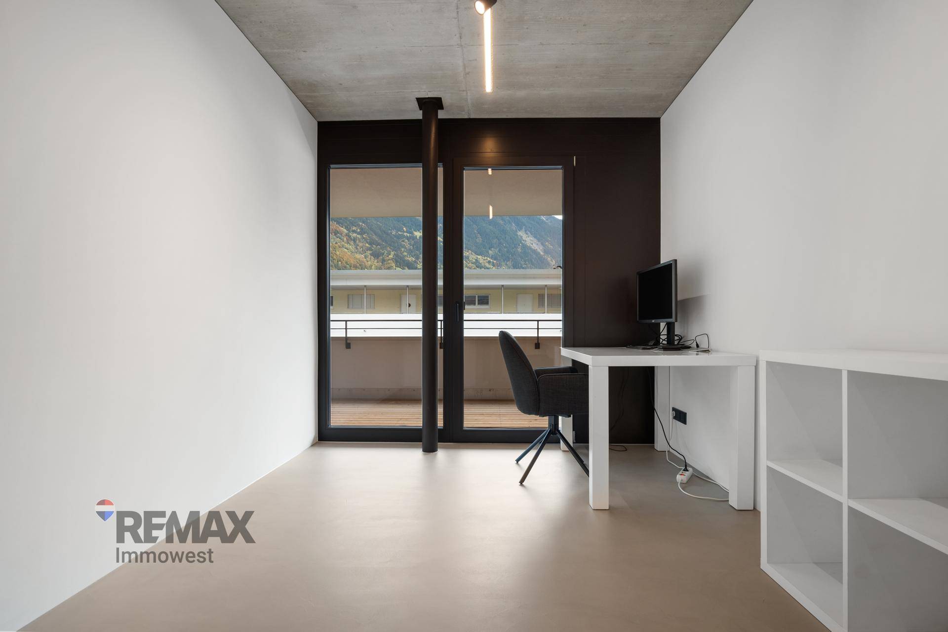 Helles Arbeitszimmer mit Schreibtisch, Regal und Zugang zu einem Balkon mit Bergblick.