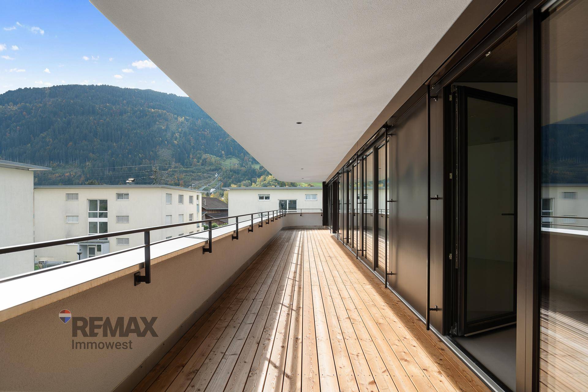 Langer Holzbalkon mit moderner Brüstung und weitem Blick auf die umliegende Berglandschaft.