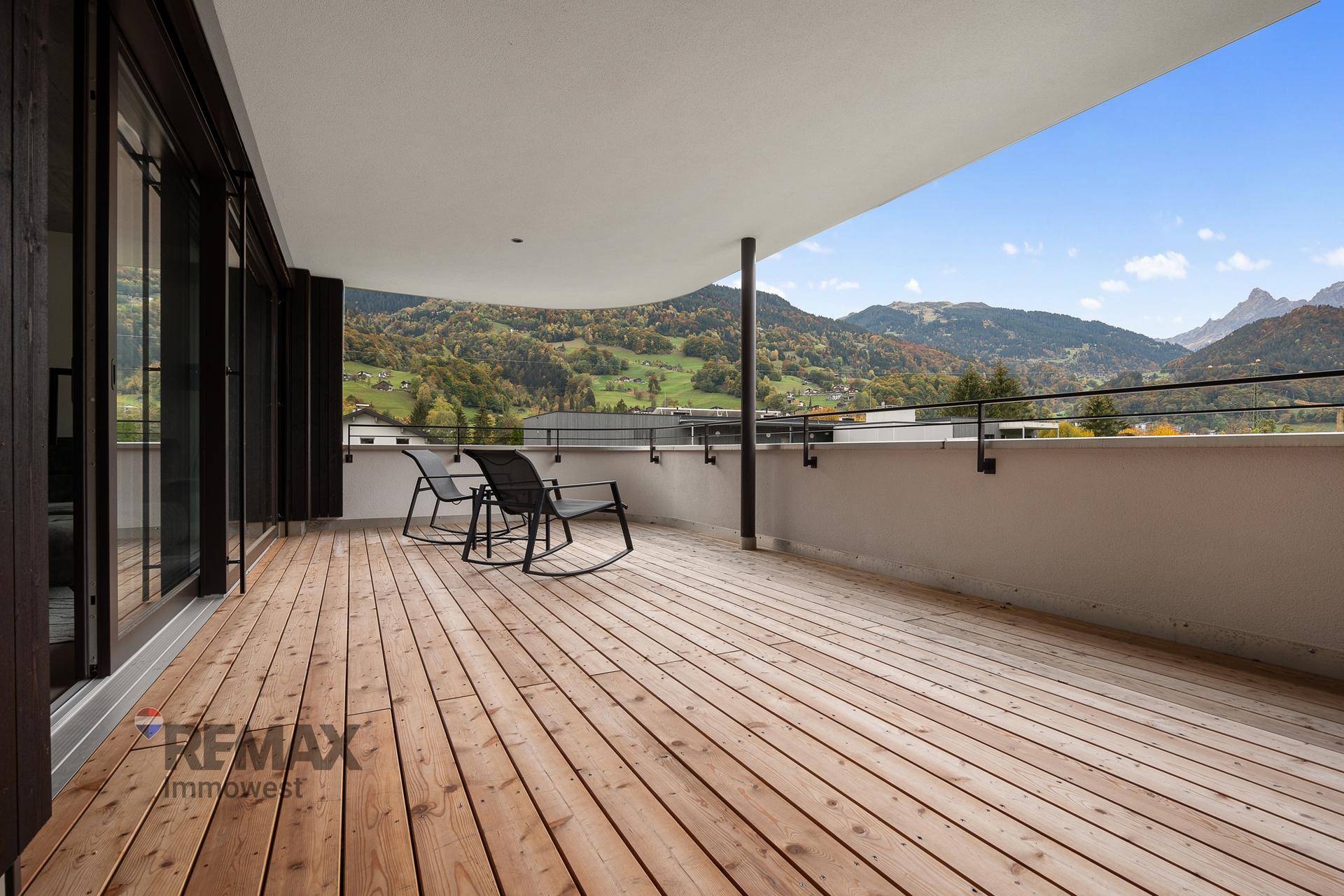 Großer Balkon mit Holzbelag und zwei Stühlen, ideal zum Entspannen mit Bergblick.