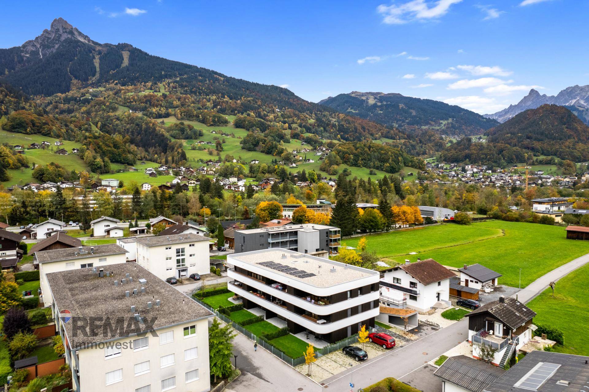 Luftaufnahme eines modernen Wohngebäudes mit Flachdach und Balkonen, eingebettet in eine grüne Berglandschaft.