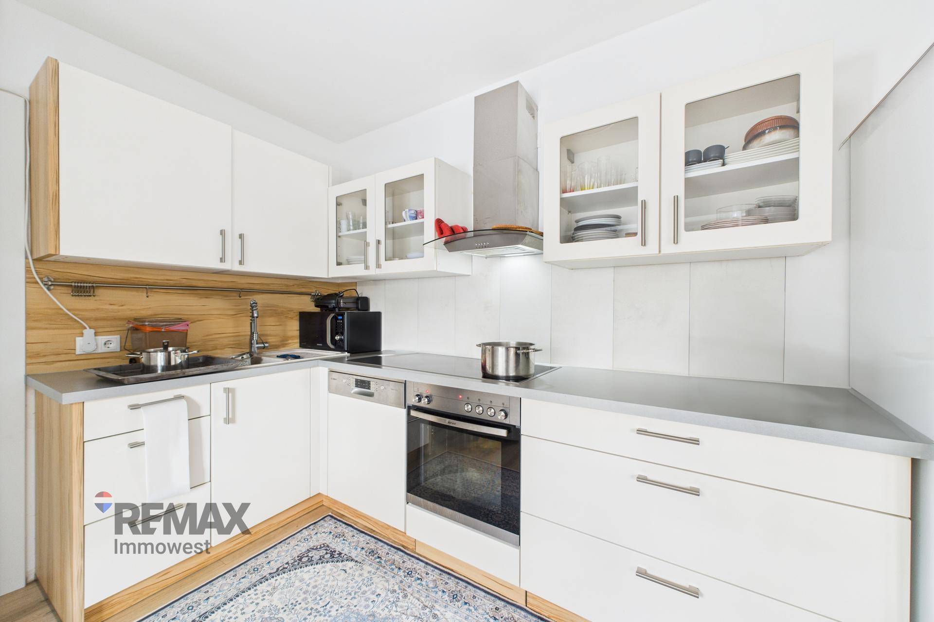 Funktionale Küche mit weißen Schränken, Holzdetails und modernen Geräten, gut ausgestattet.
