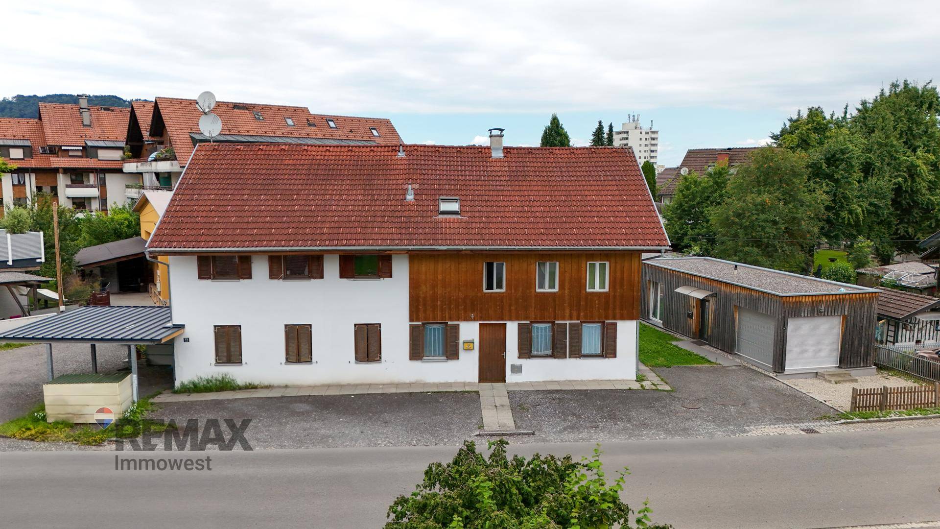 Traditionelles Wohnhaus mit weißer Fassade, Holzverkleidung und rotem Ziegeldach, umgeben von Grün.