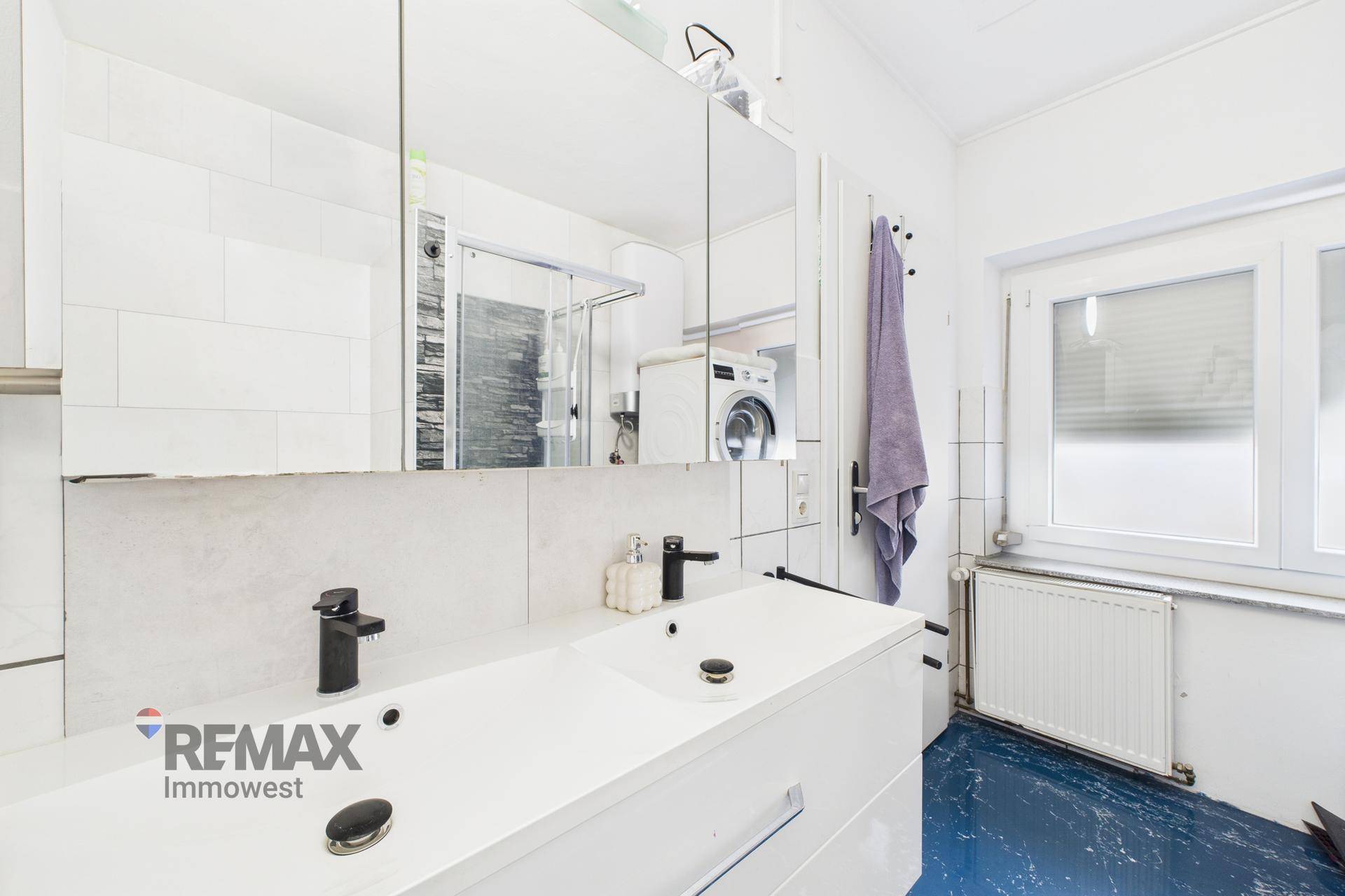 Helles Badezimmer mit Doppelwaschbecken, Spiegelschrank und Fenster, inklusive Waschmaschine.