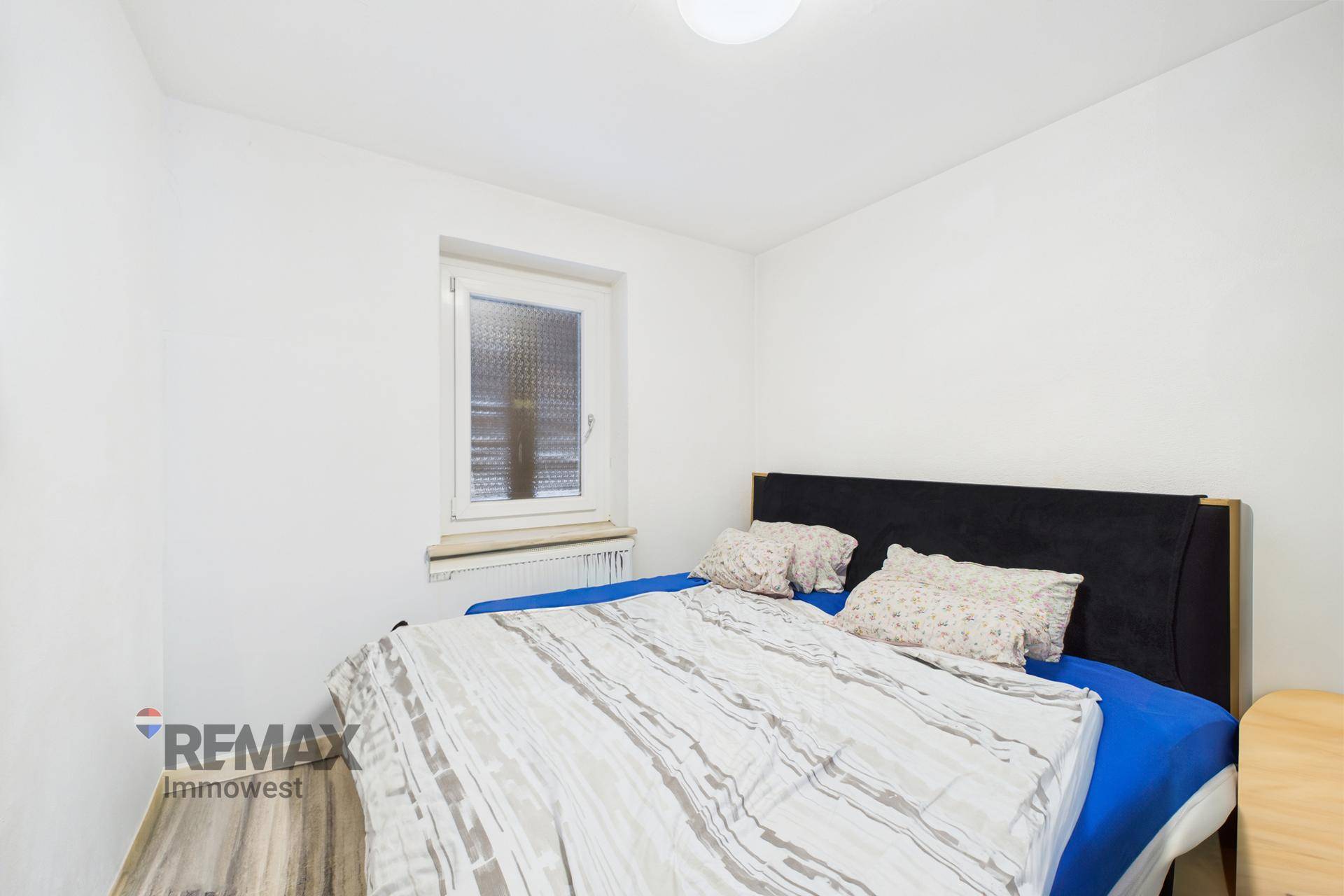 Schlafzimmer mit Doppelbett, weiß gestrichenen Wänden und Fenster, einfach und hell.
