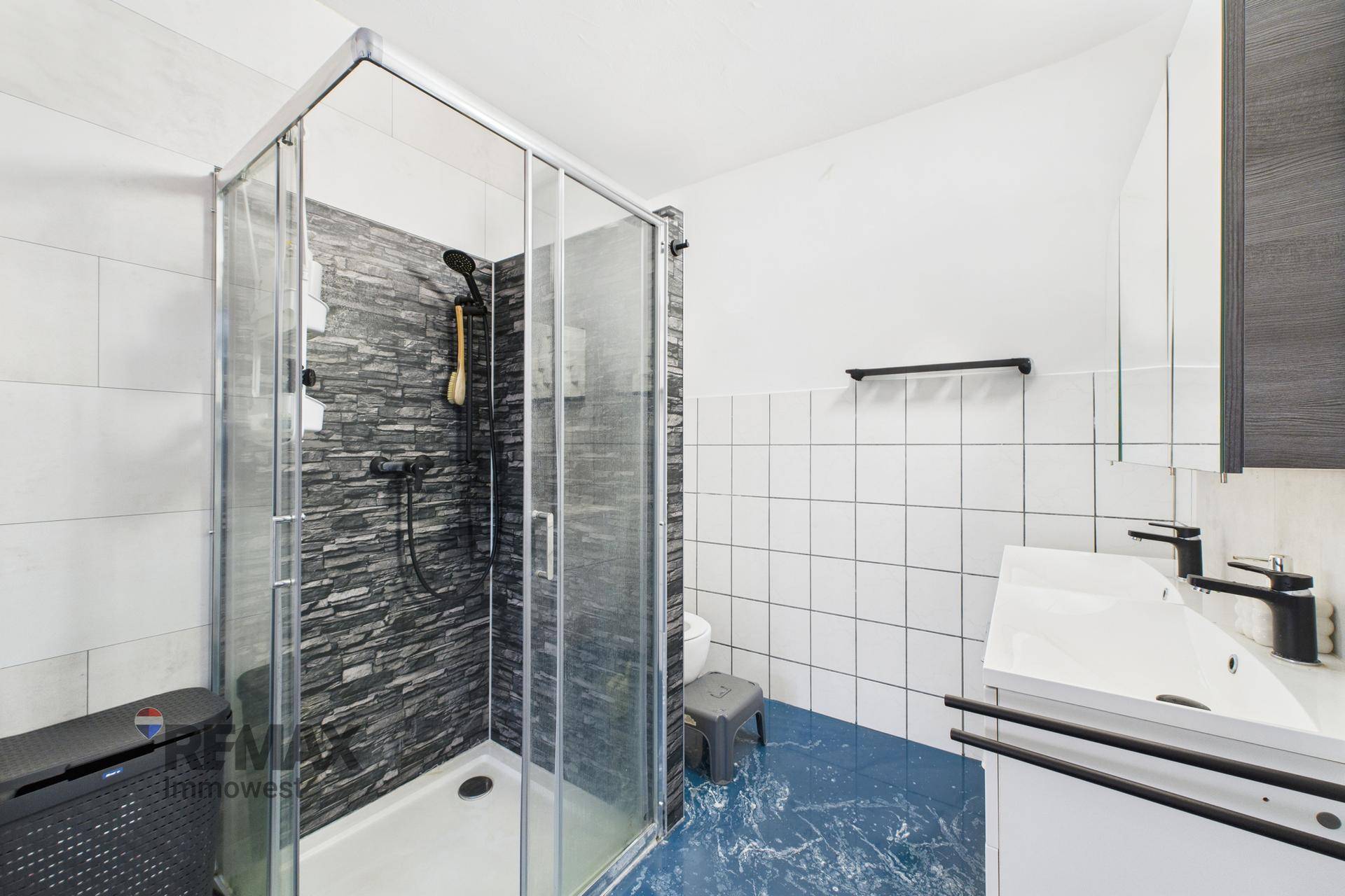 Modernes Badezimmer mit Duschkabine, dunklen Fliesen und weißem Waschbecken, funktional gestaltet.