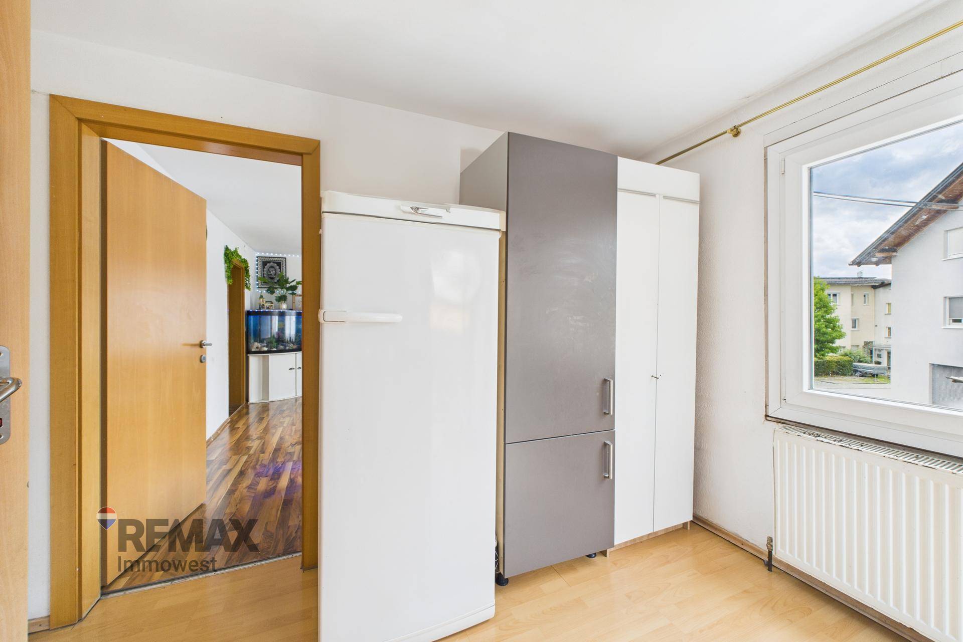 Flur oder Abstellraum mit Kühlschrank und Schränken, hell durch ein Fenster.