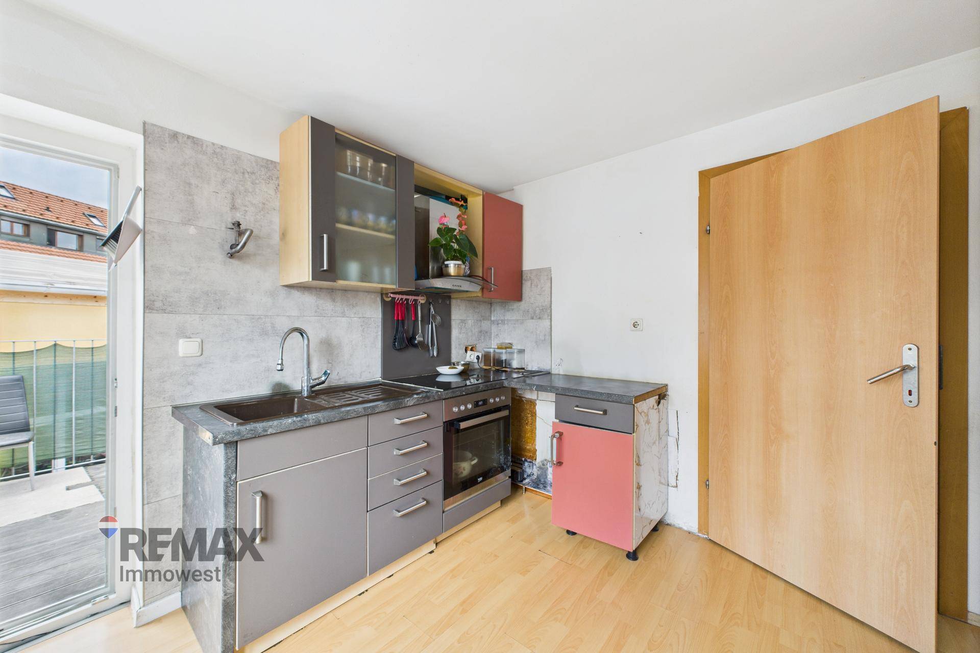 Kleine Küche mit grauen und roten Schränken, integrierten Geräten und Zugang zur Terrasse.