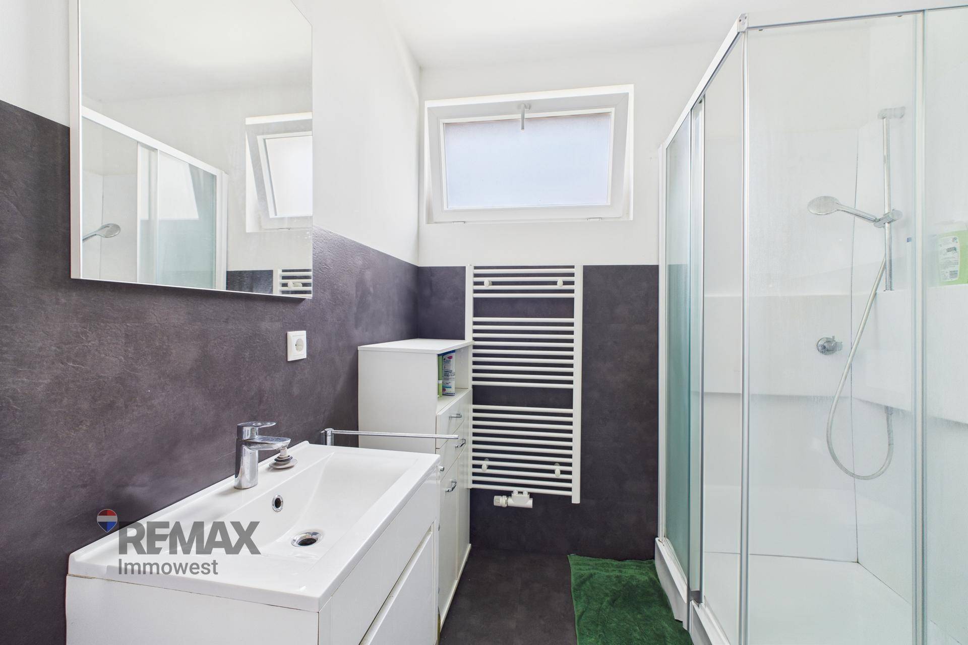 Modernes Badezimmer mit Duschkabine, Waschbecken und beheiztem Handtuchhalter, hell und sauber.