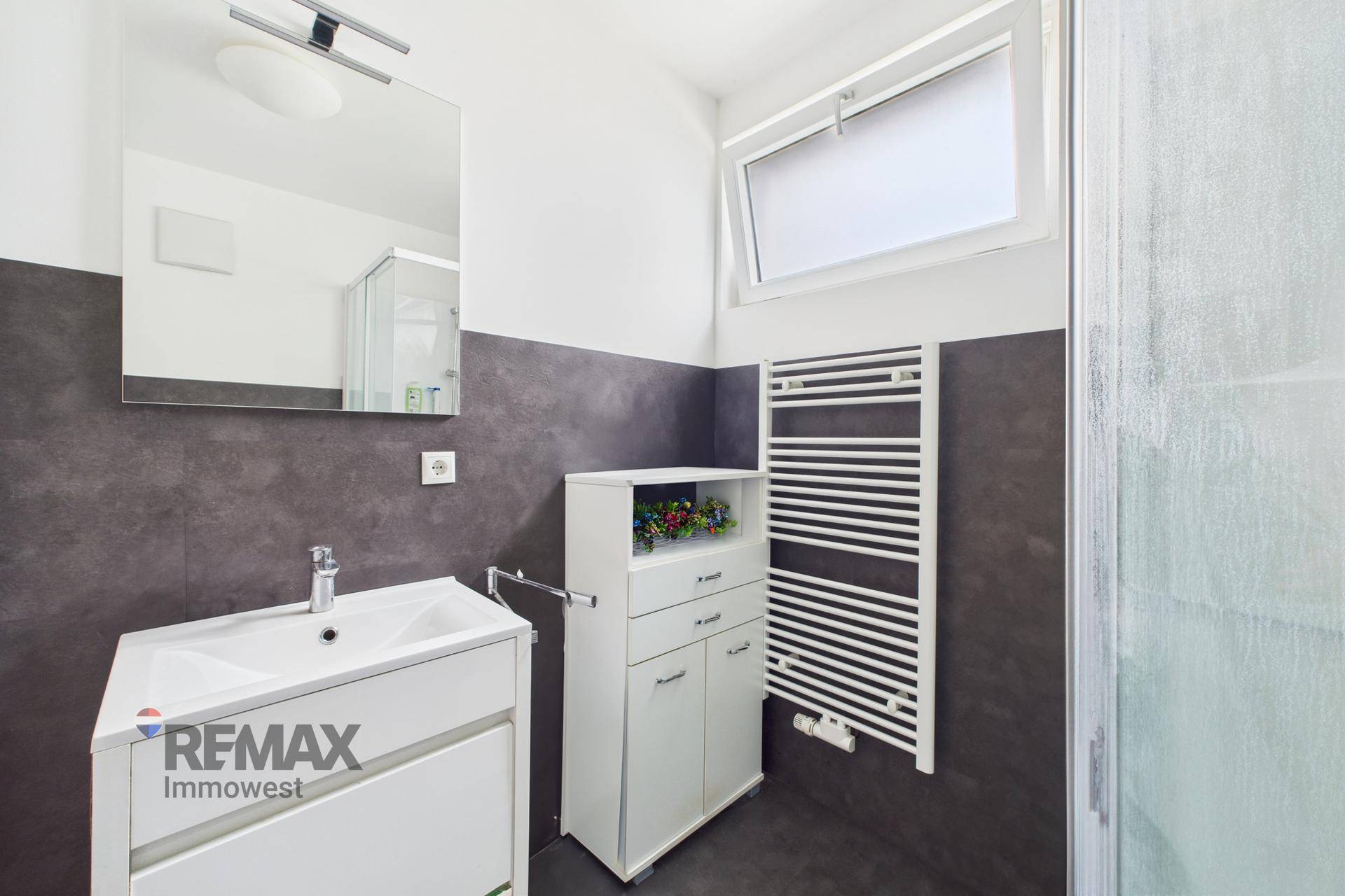 Helles Badezimmer mit Waschbecken, Spiegelschrank und Fenster, beheizter Handtuchhalter.