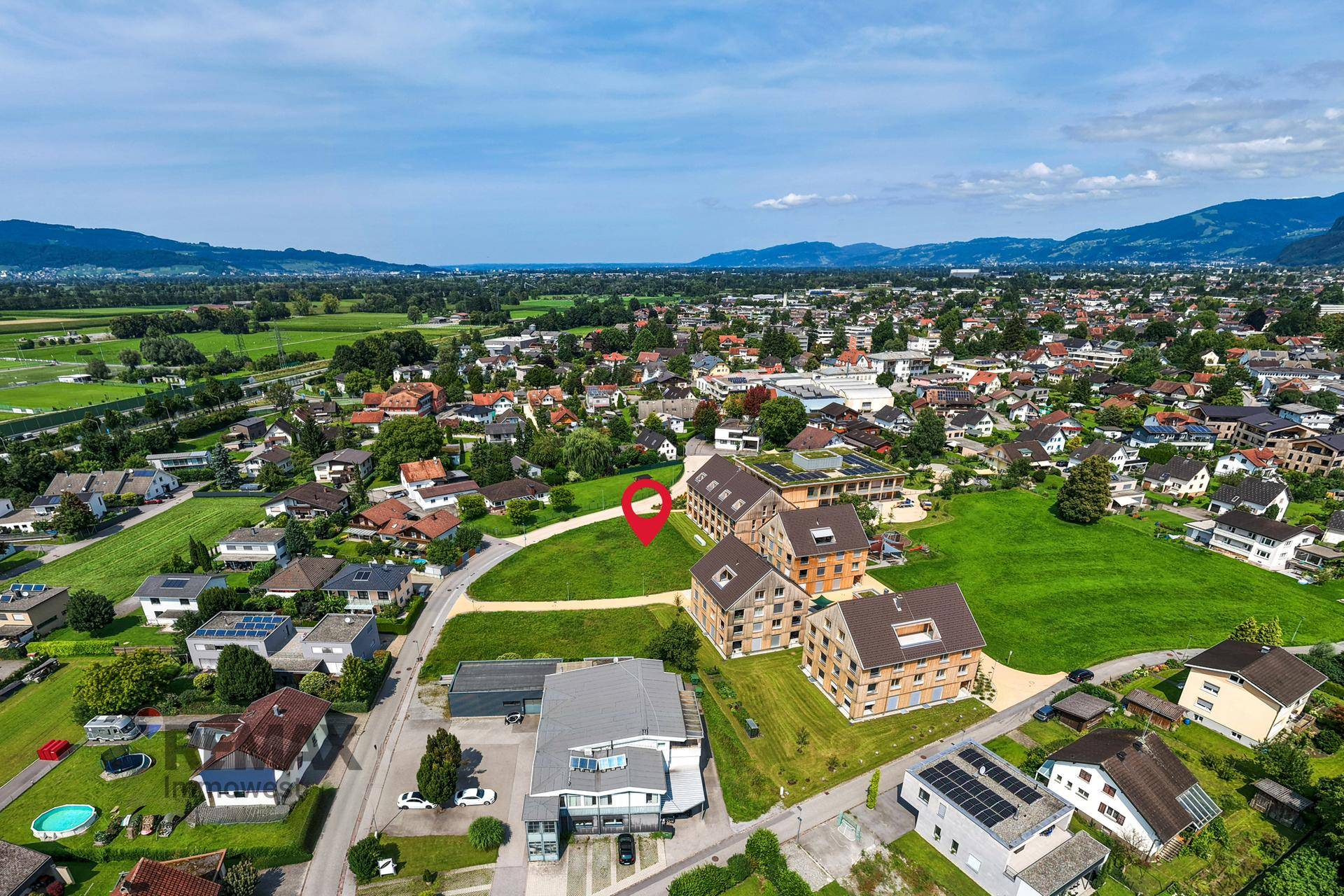 Weitläufige Luftaufnahme einer Siedlung mit Bergen im Hintergrund und einem markierten Grundstück.