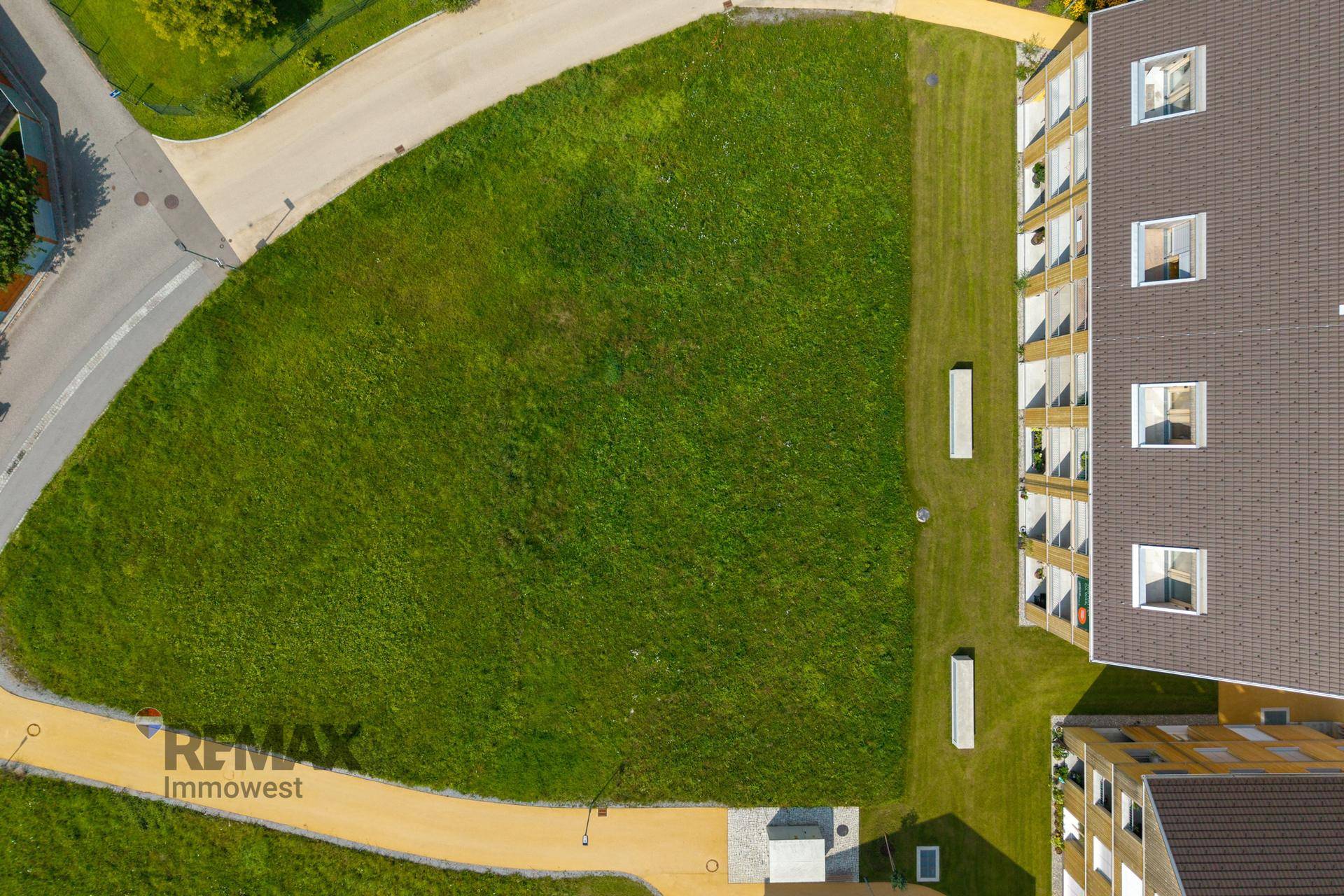 Senkrechte Luftaufnahme eines unbebauten Grundstücks mit angrenzendem modernen Wohngebäude.