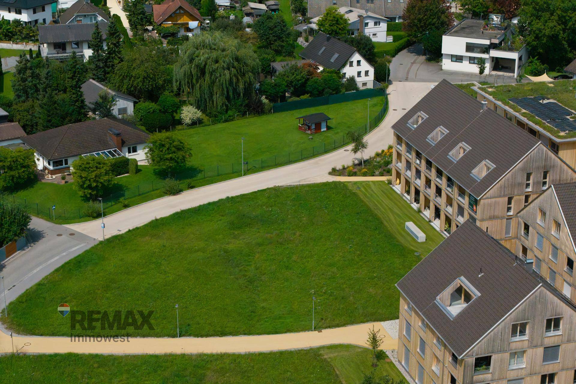 Luftaufnahme eines großen grünen Grundstücks umgeben von Wohngebäuden und Bäumen.