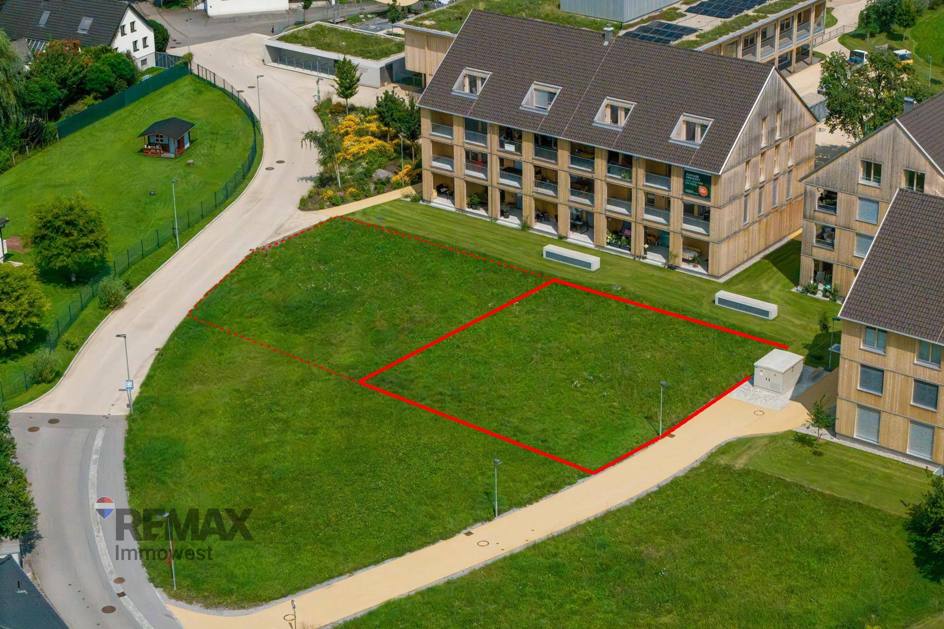 Luftaufnahme eines markierten Baugrundstücks neben einem modernen Wohnhaus mit Balkonen.