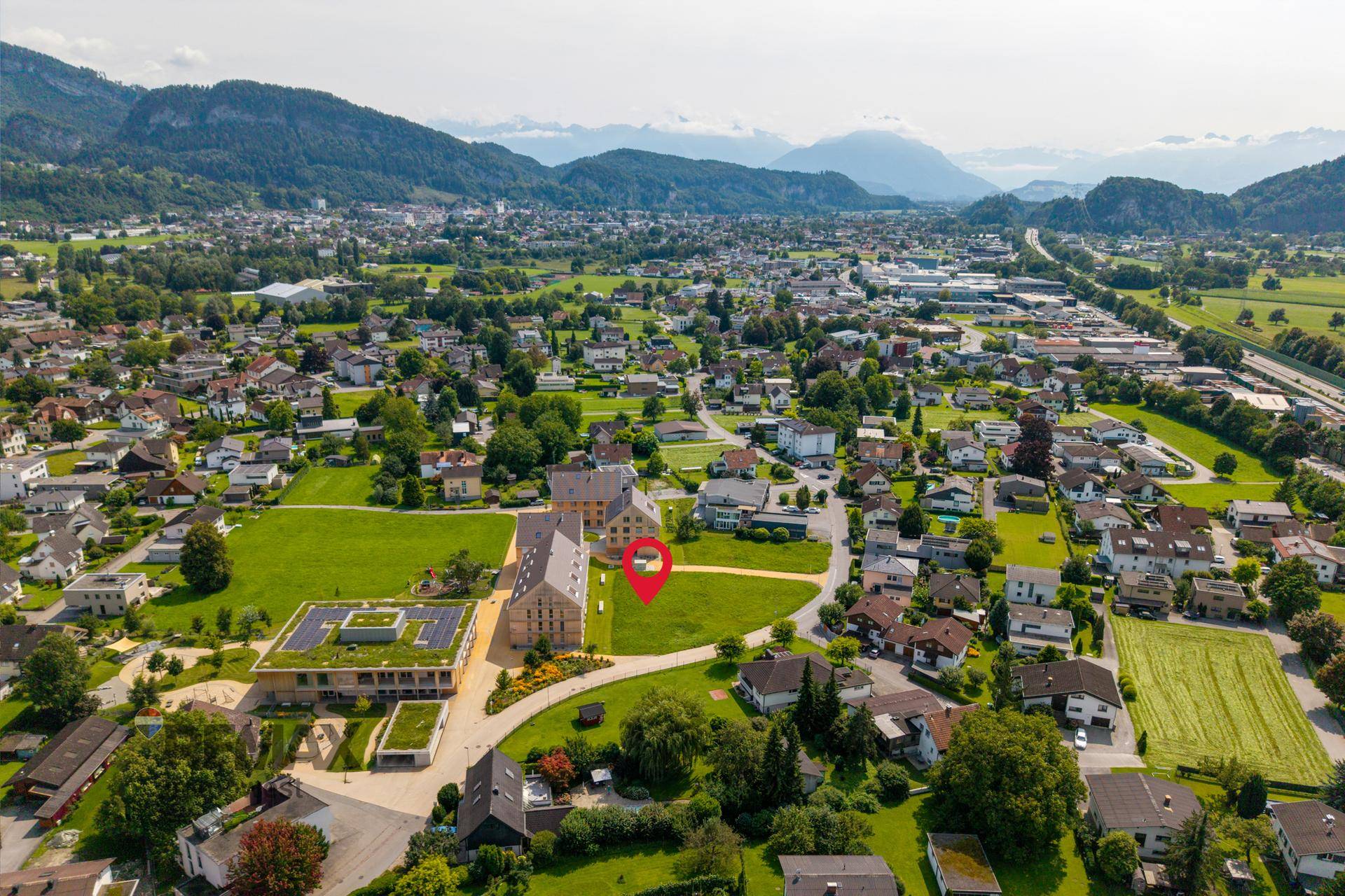 Weitläufige Luftaufnahme einer ländlichen Siedlung mit Bergen und einem markierten Grundstück.
