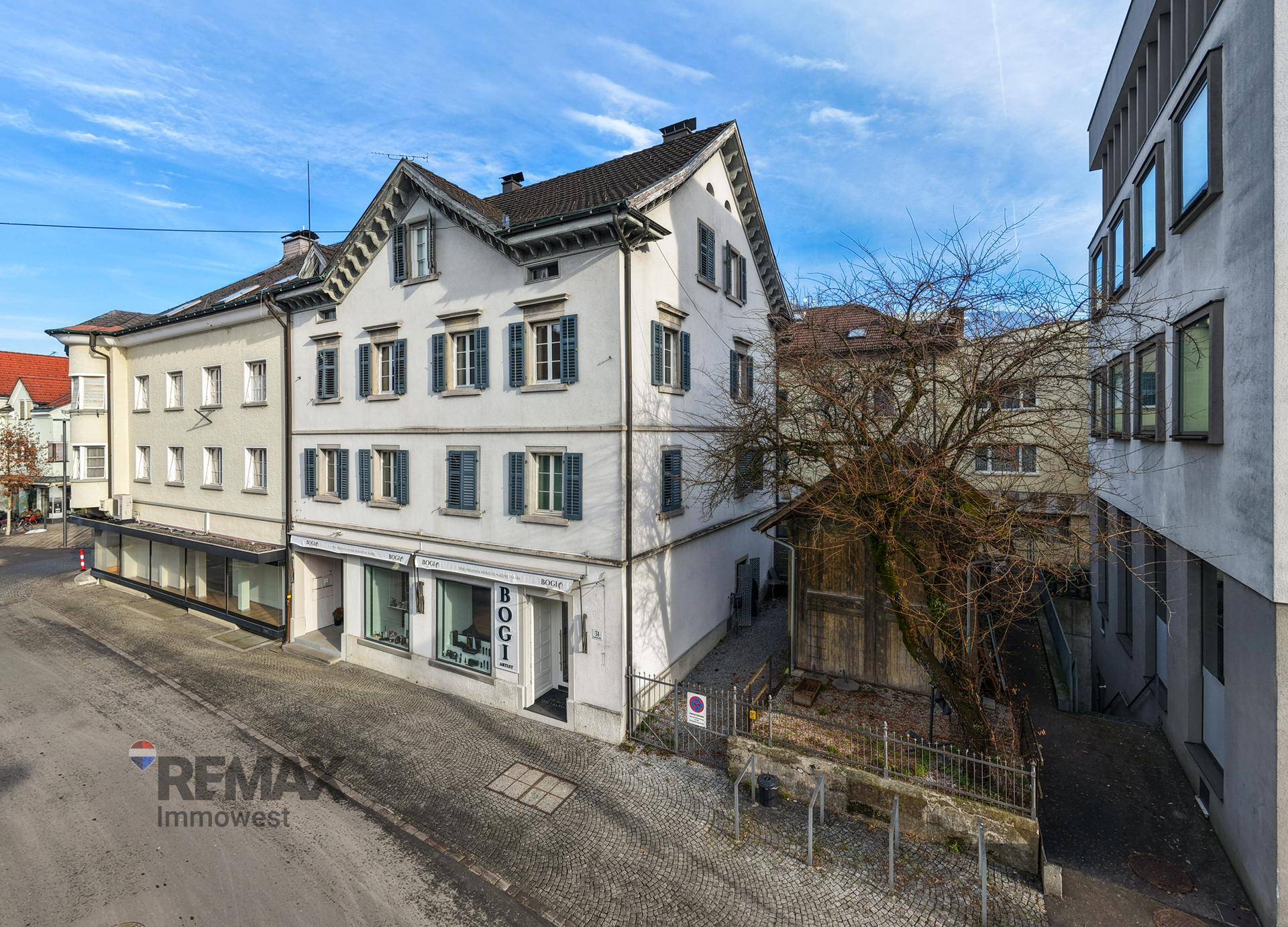 Historisches Gebäude mit markantem Dach und Ladenlokal in einer städtischen Umgebung.