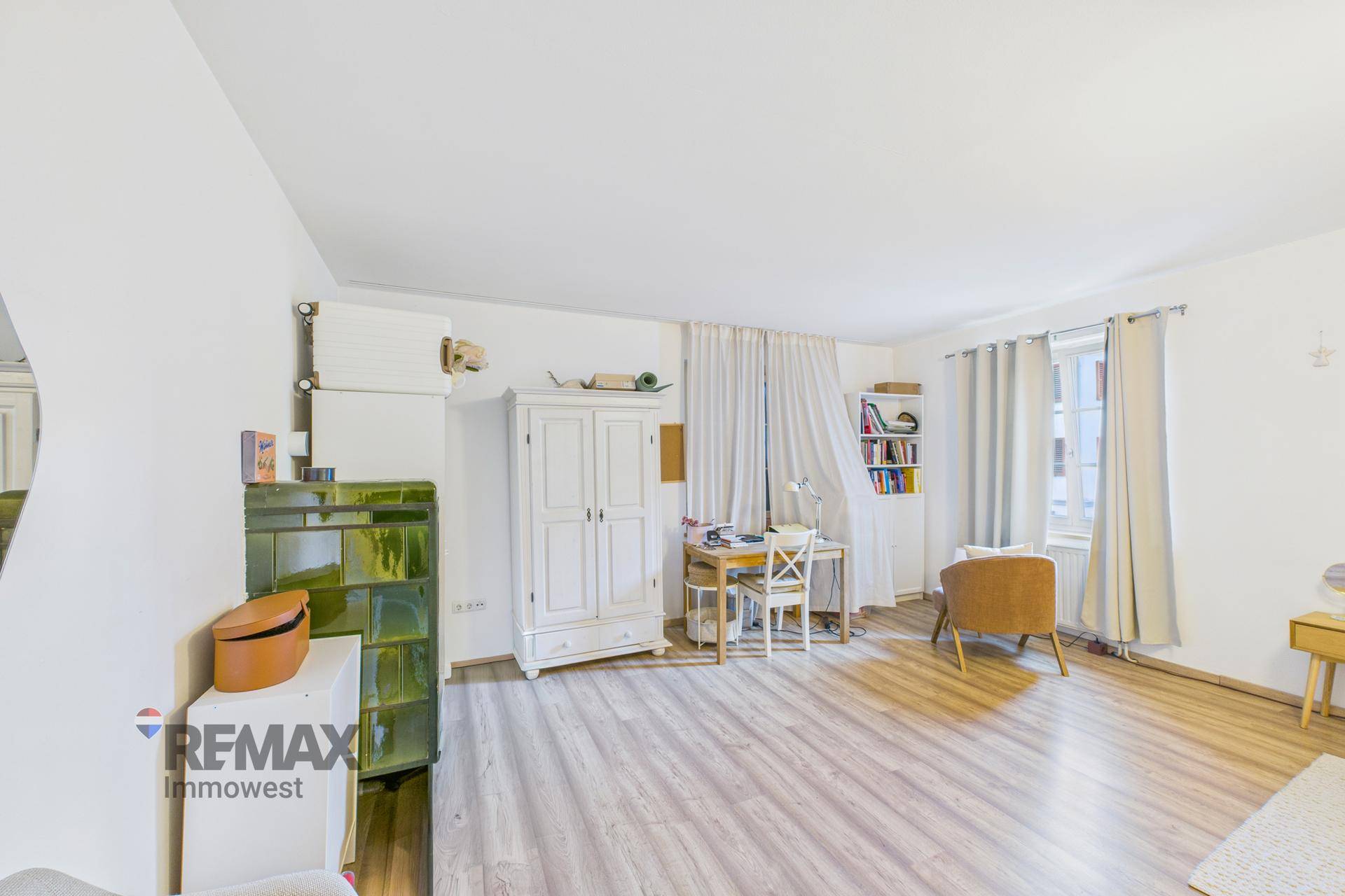 Geräumiges Wohnzimmer mit Kachelofen, Schreibtisch und hellem Laminatboden.