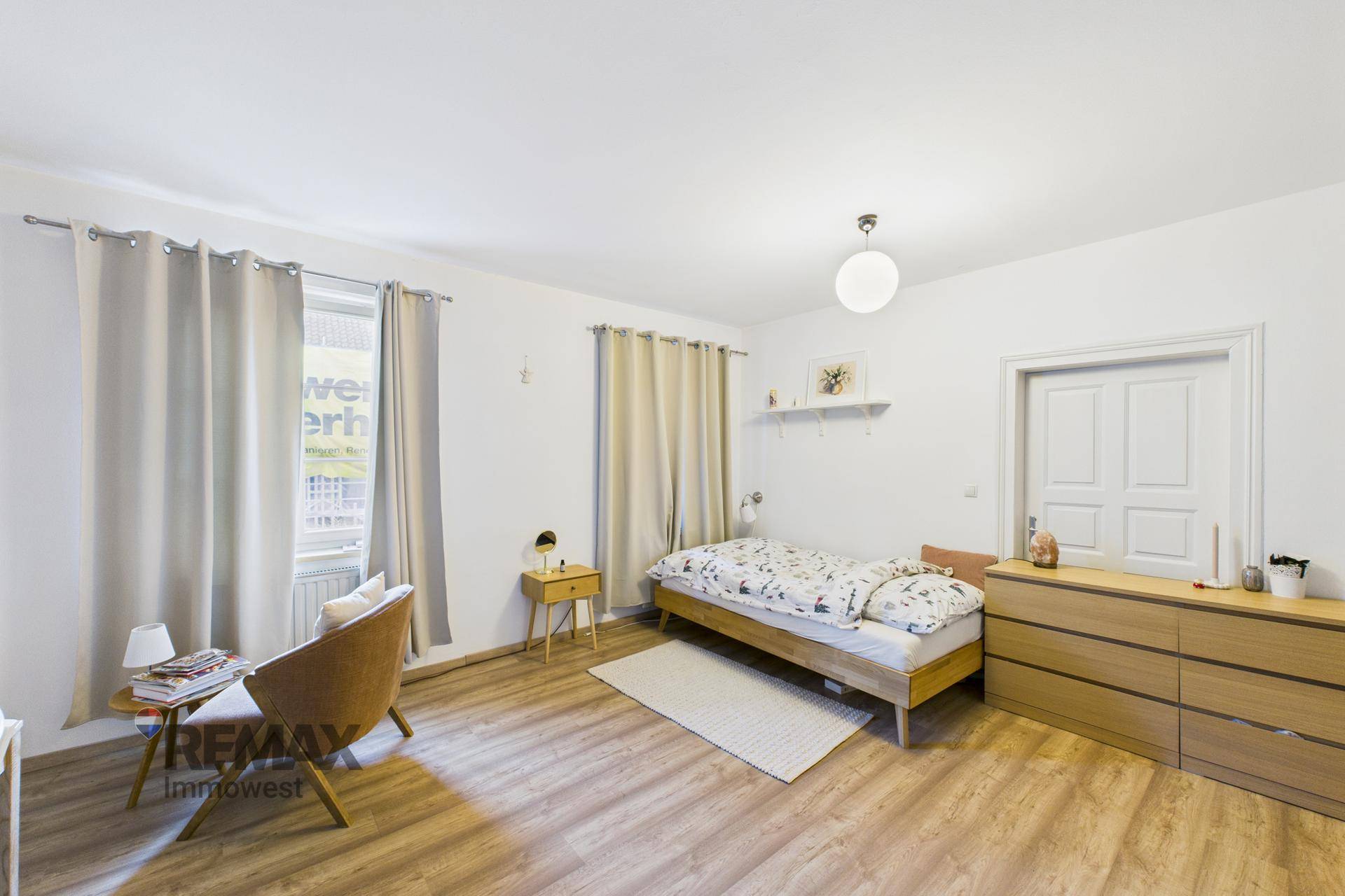 Helles Schlafzimmer mit Einzelbett, Kommode und modernem Laminatboden.