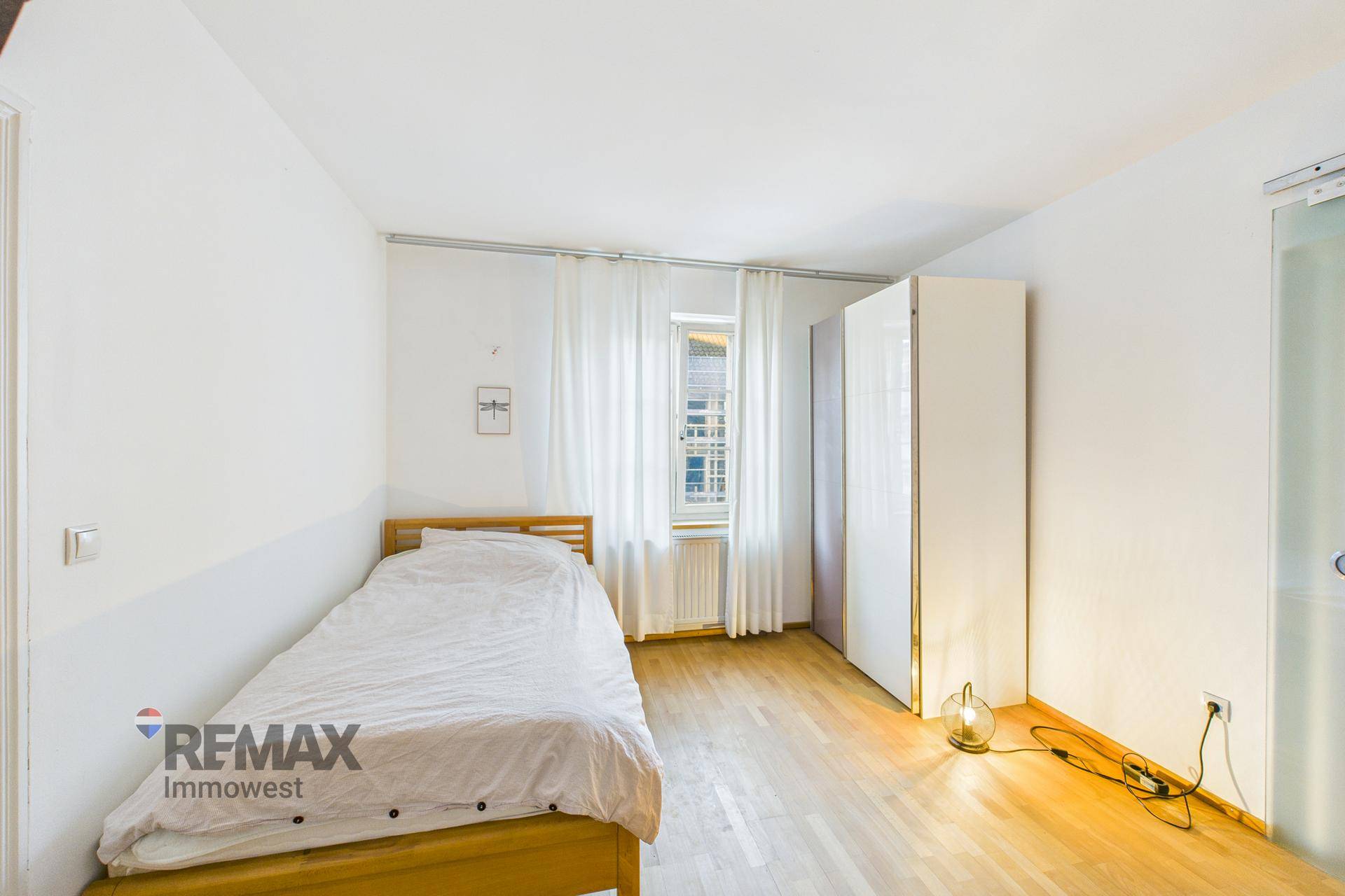 Einfaches Schlafzimmer mit Holzbett, weißem Kleiderschrank und hellem Holzfußboden.