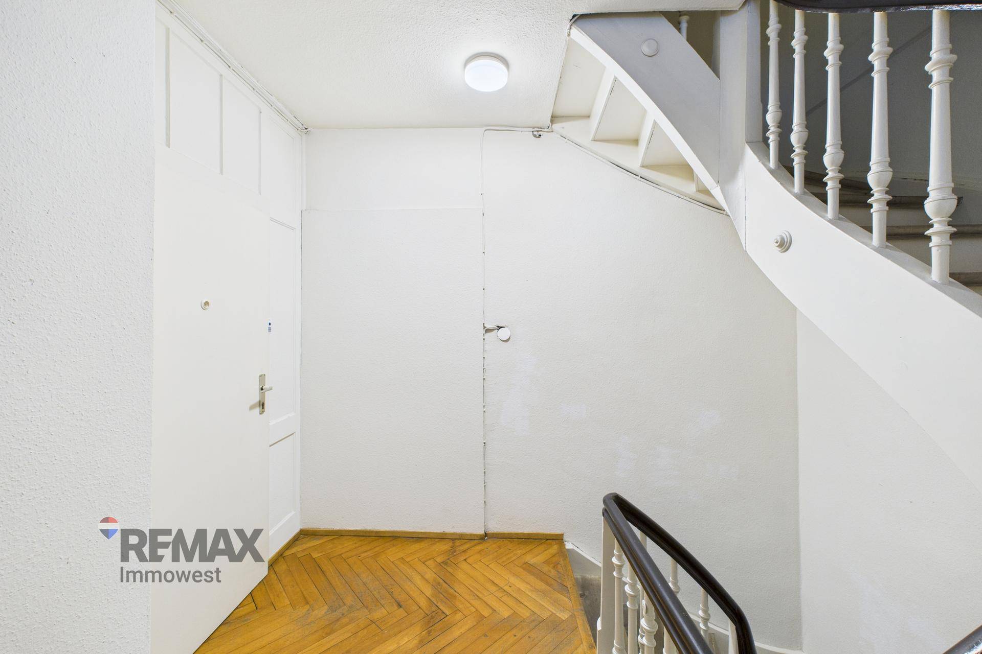 Treppenhaus mit Holzparkettboden und einer geschwungenen Holztreppe mit Geländer.