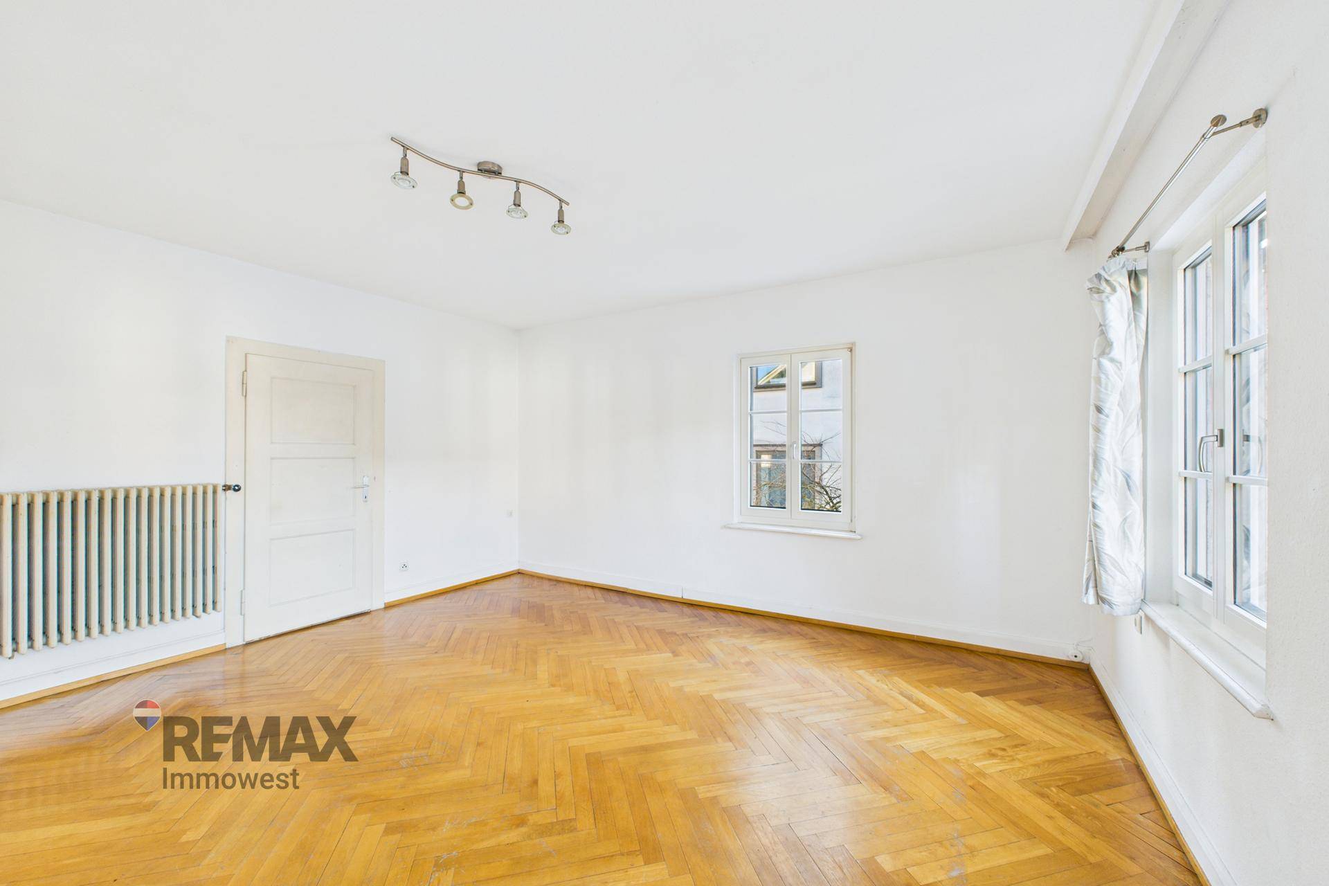 Helles Wohnzimmer mit Fischgrätparkettboden, einem Fenster und einem Heizkörper.