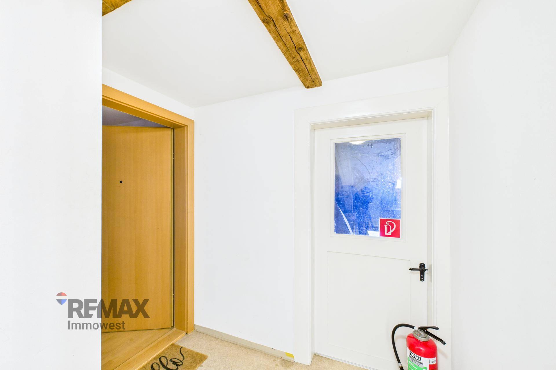 Eingangsbereich mit Holzbalken an der Decke, Holztüren und einem Feuerlöscher.