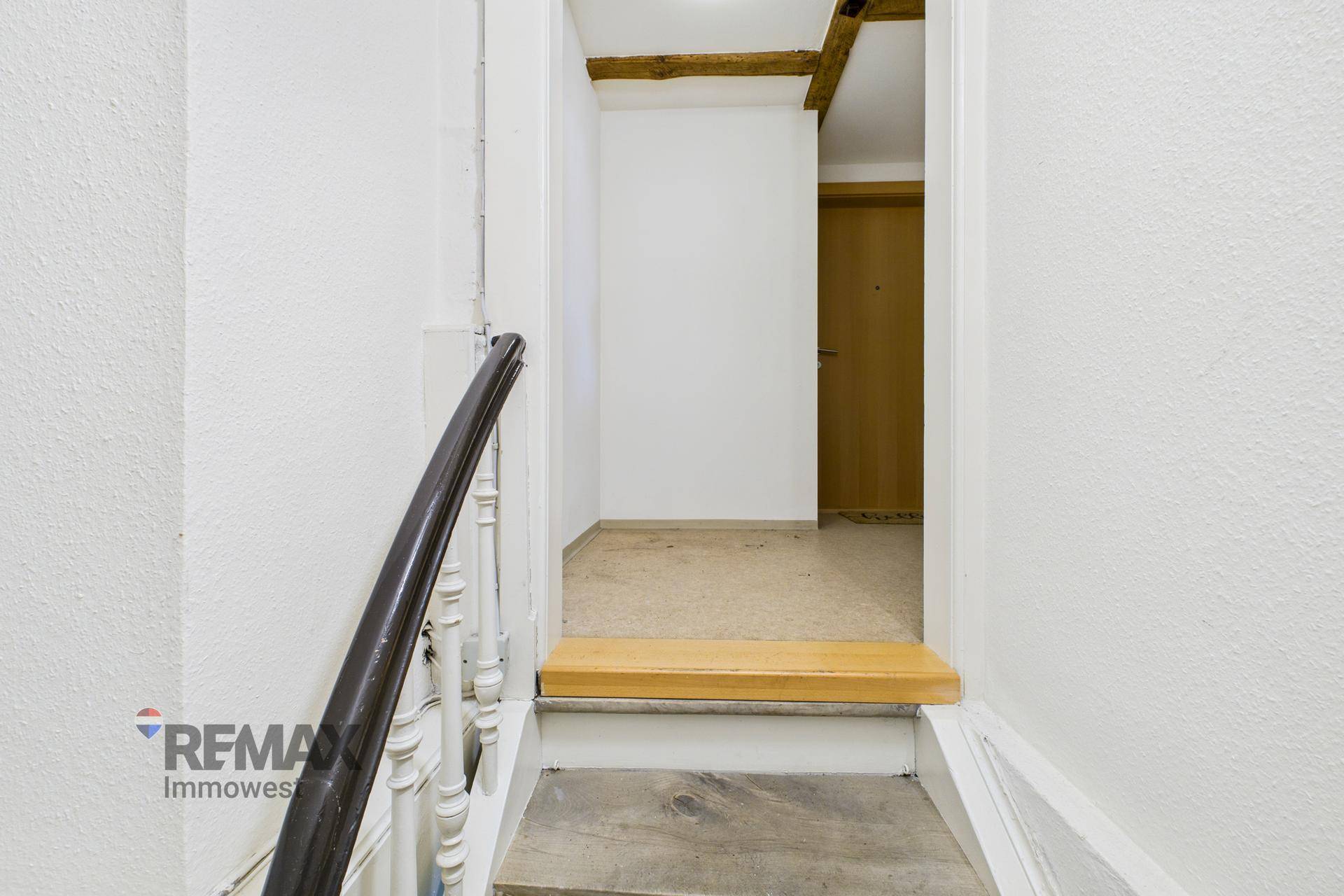 Treppenaufgang mit Holzgeländer und sichtbaren Holzbalken an der Decke.