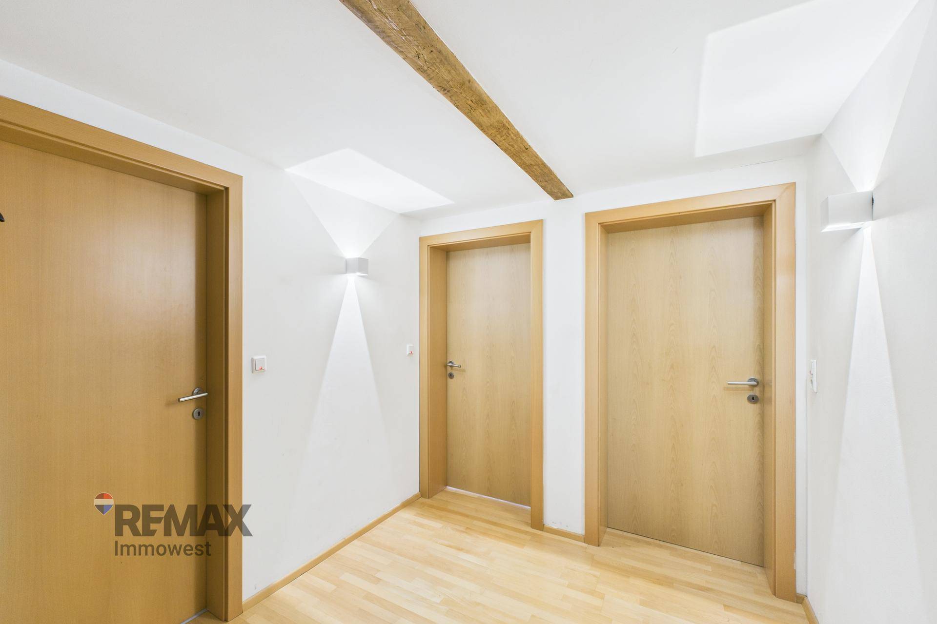 Heller Flur mit Holzbalken an der Decke, Holztüren und Wandleuchten.