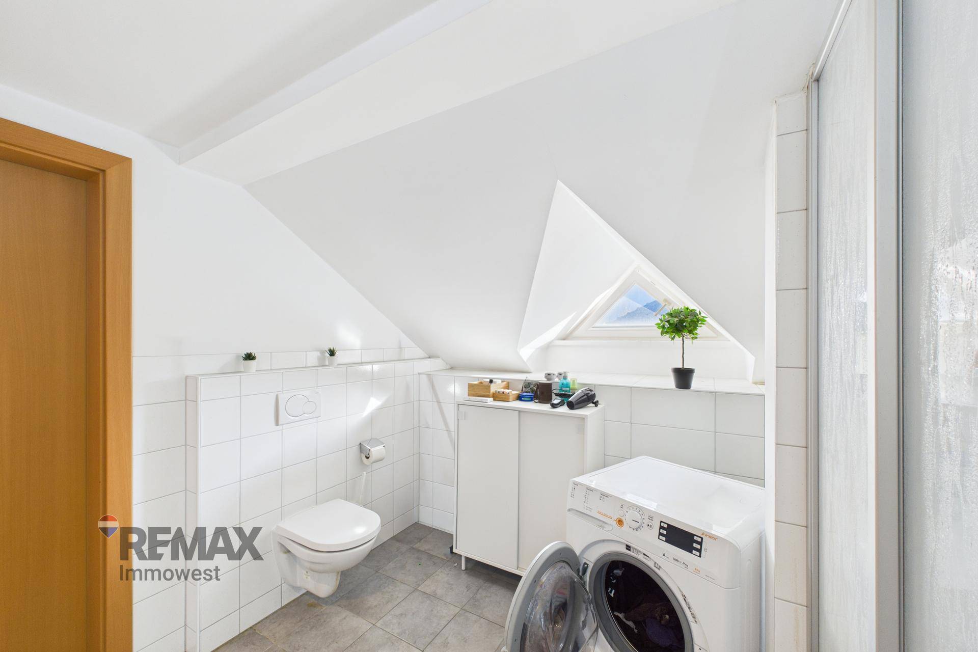 Dachschrägen-Badezimmer mit WC, Waschmaschine und Dachfenster für natürliches Licht.
