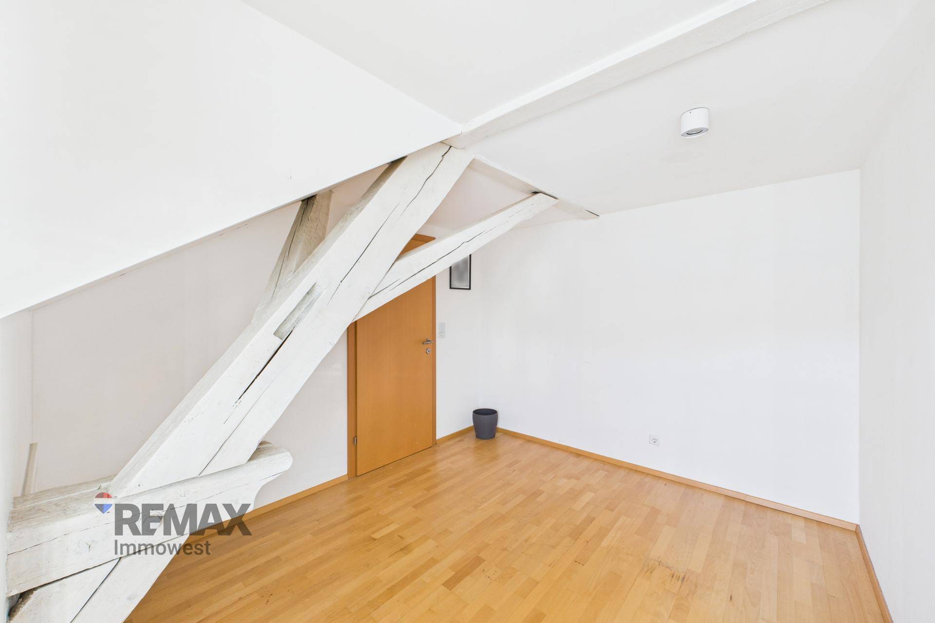 Heller Raum mit Holzboden und markanten Holzbalken, die die Dachschräge betonen.