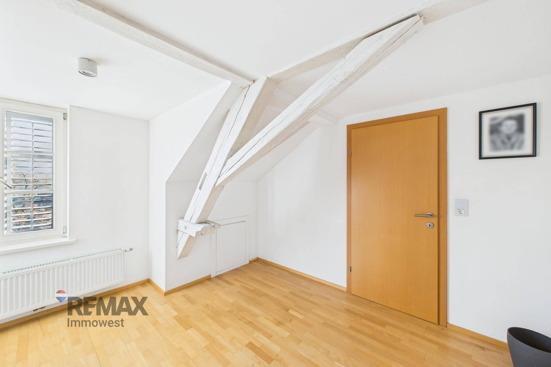 Geräumiger Raum mit Holzboden, freiliegenden Holzbalken und schrägen Wänden.