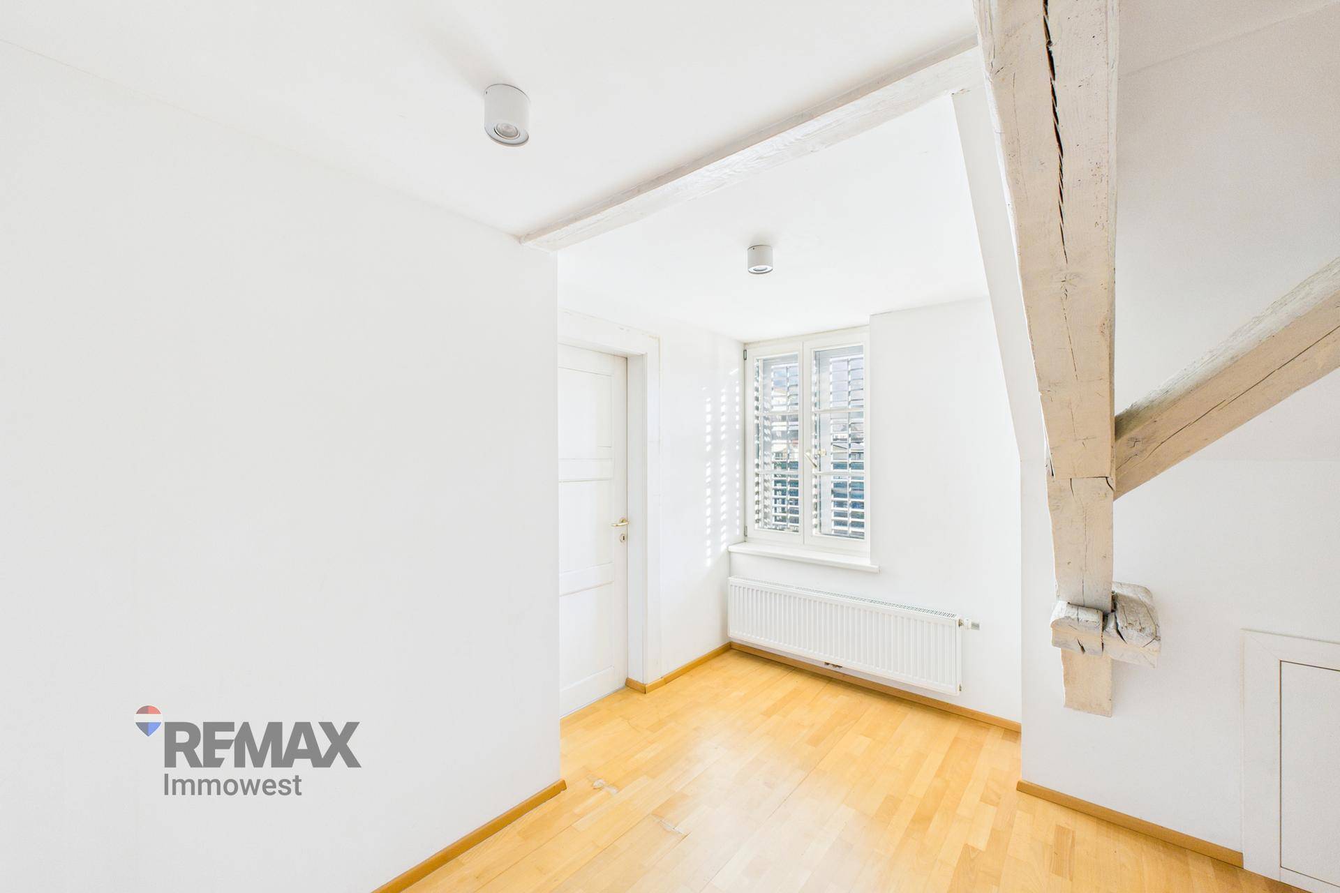 Heller Raum mit Holzboden, sichtbaren Holzbalken und Fenster mit Fensterläden.