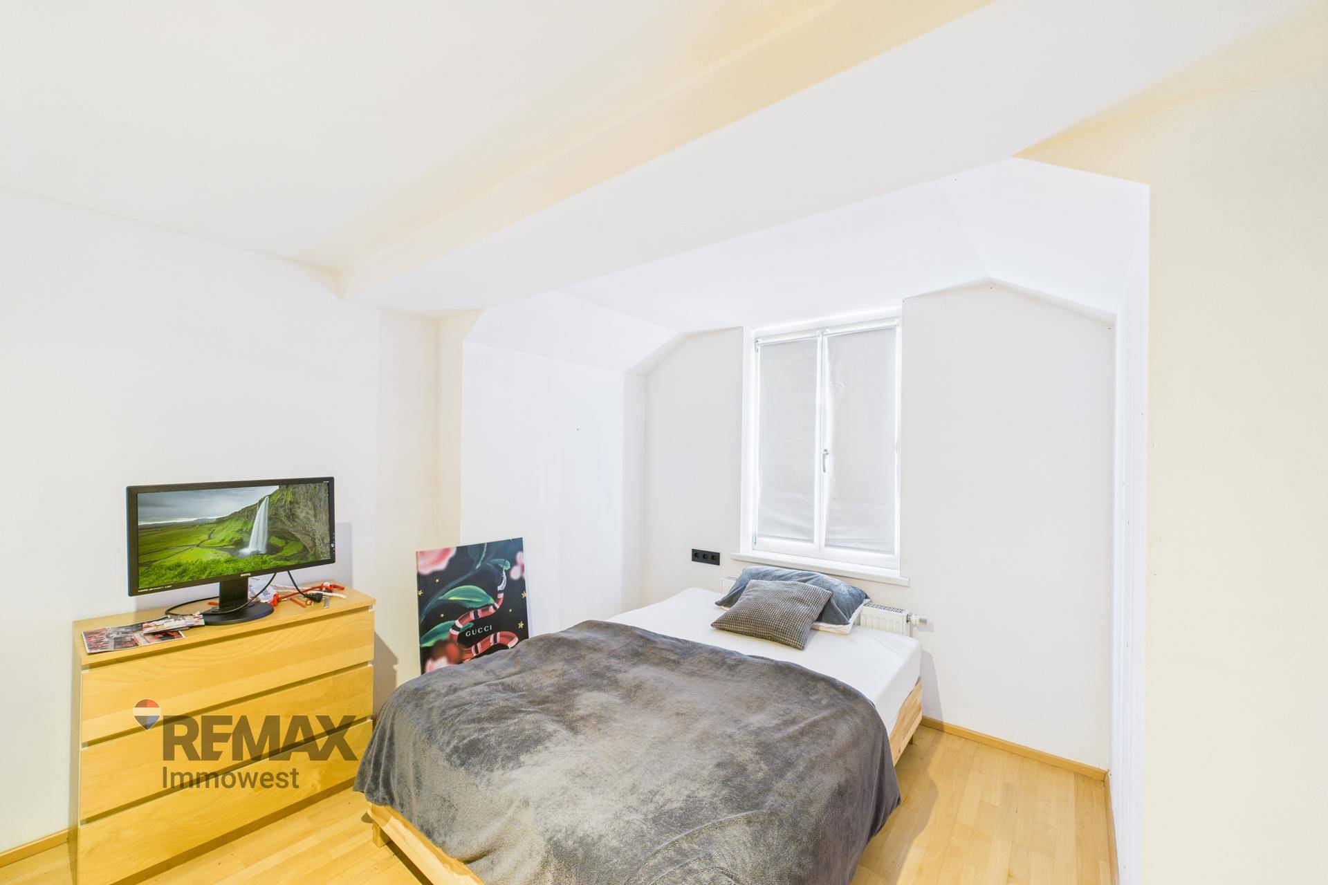 Schlafzimmer mit Holzbett, Kommode und Fernseher unter einer Dachschräge.