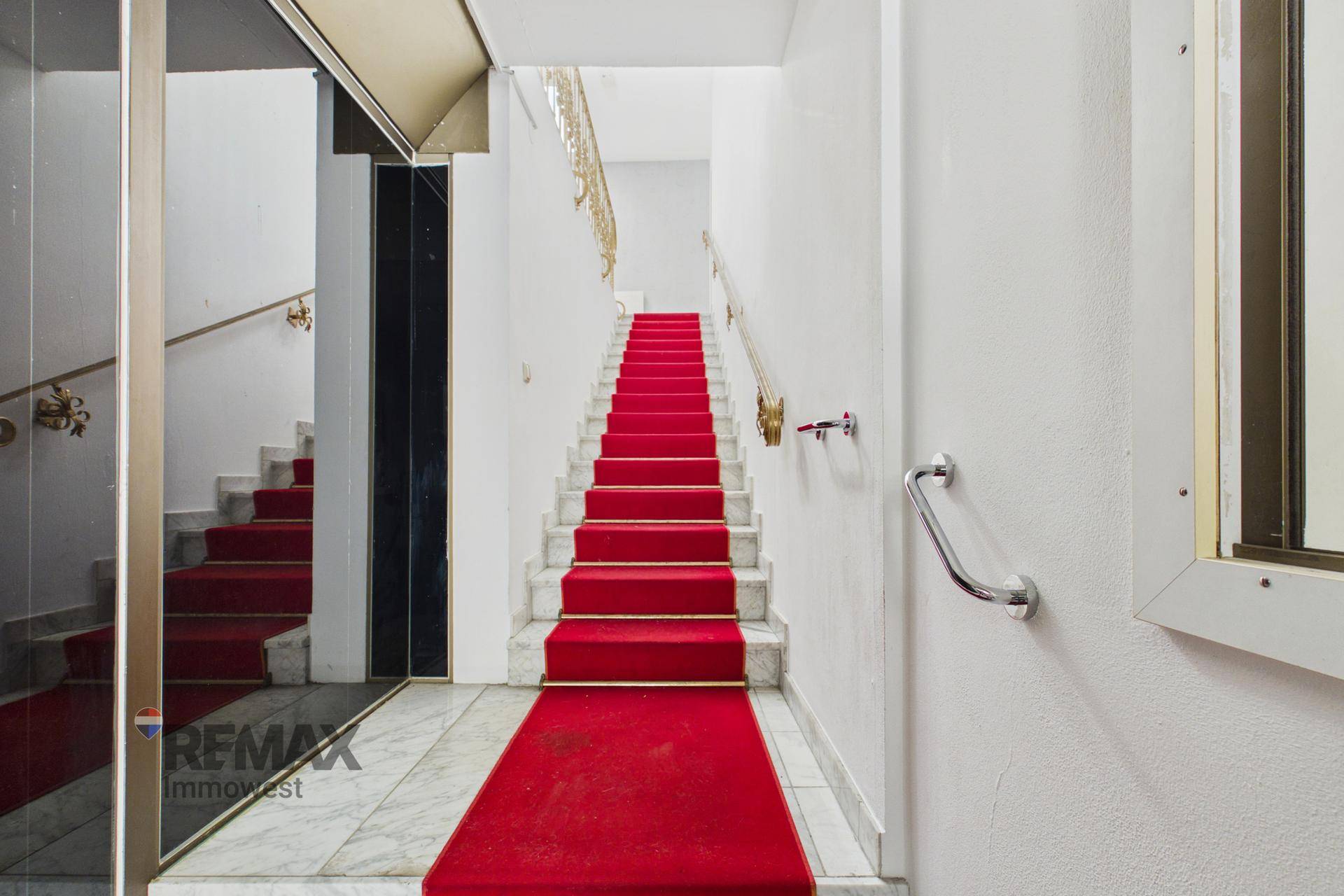 Treppenhaus mit rotem Teppichläufer, Marmorboden und elegantem goldenen Geländer.
