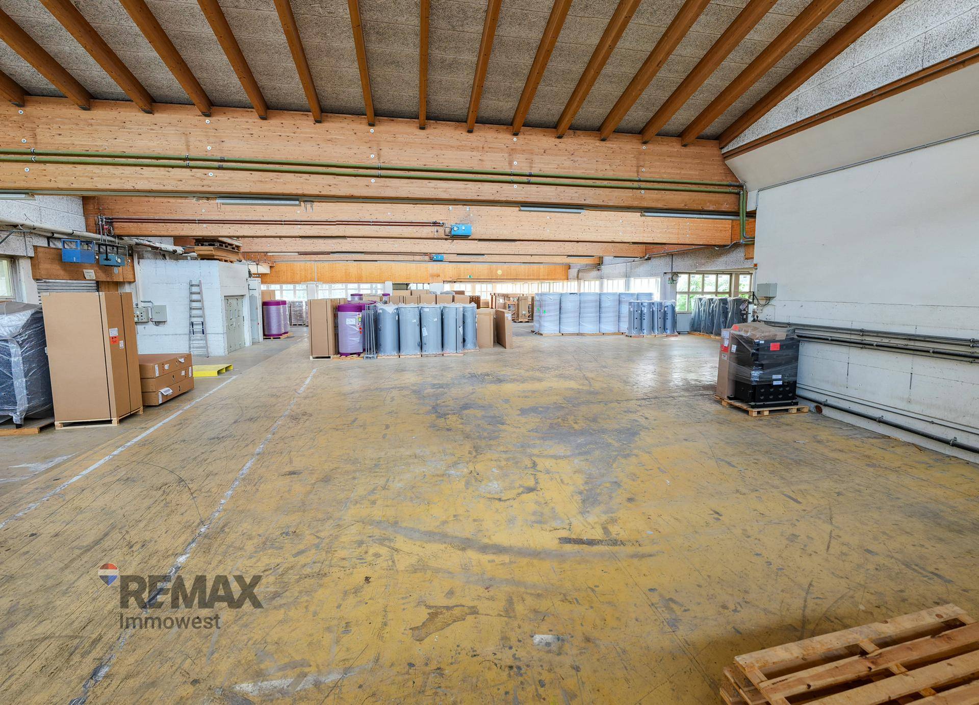 Geräumige Lagerhalle mit hoher Decke, Holzbalkenkonstruktion und robustem Betonboden für schwere Lasten.