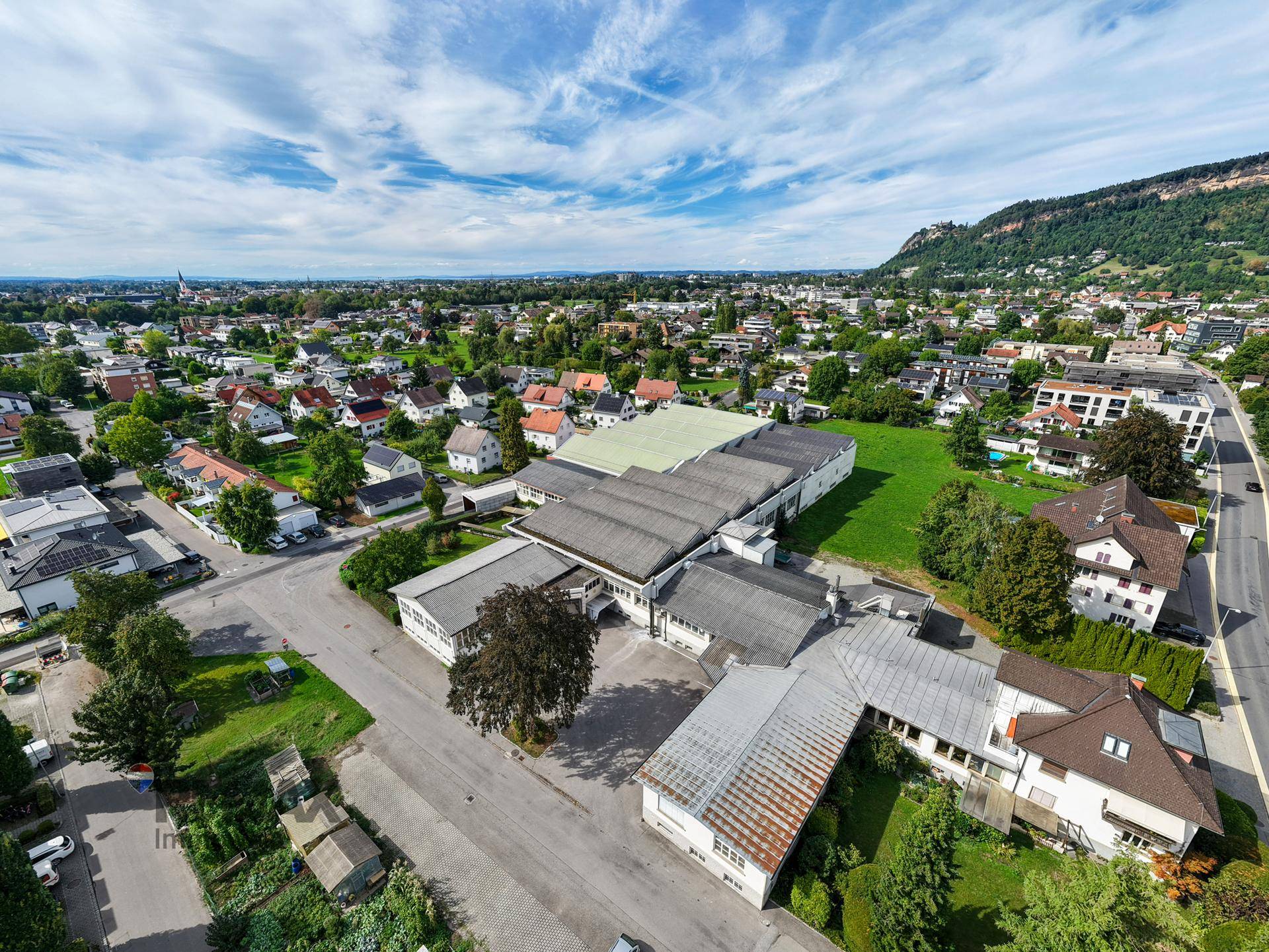 Weitläufige Luftaufnahme des Gewerbekomplexes in einer ländlichen Umgebung mit Bergen im Hintergrund.