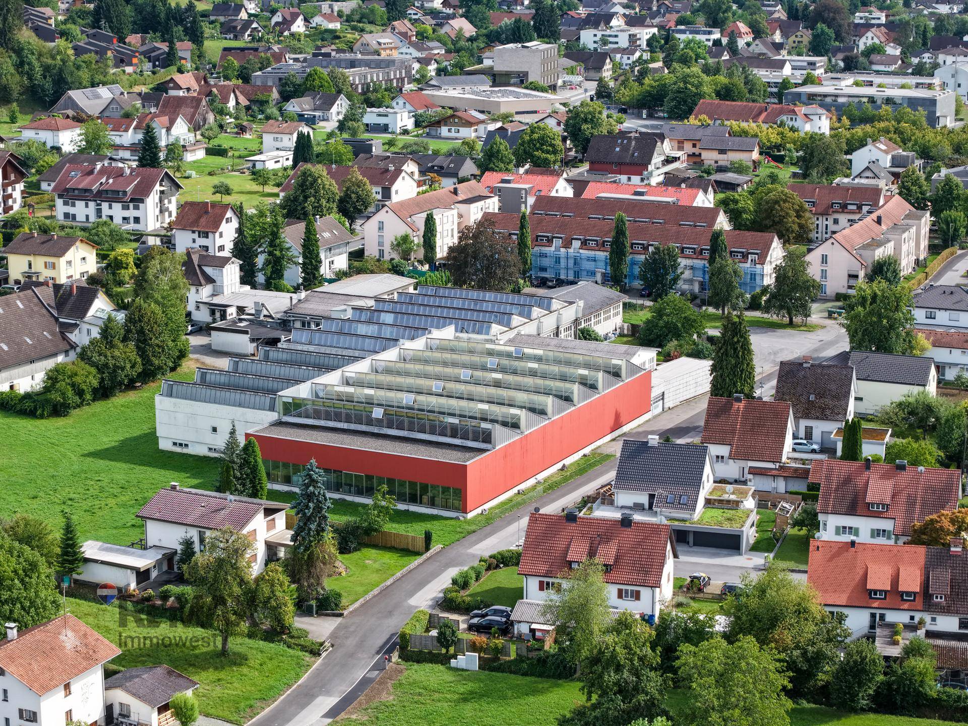 Luftaufnahme eines großen Gewerbegebäudes mit Solaranlage auf dem Dach, umgeben von Wohngebäuden und Grünflächen.