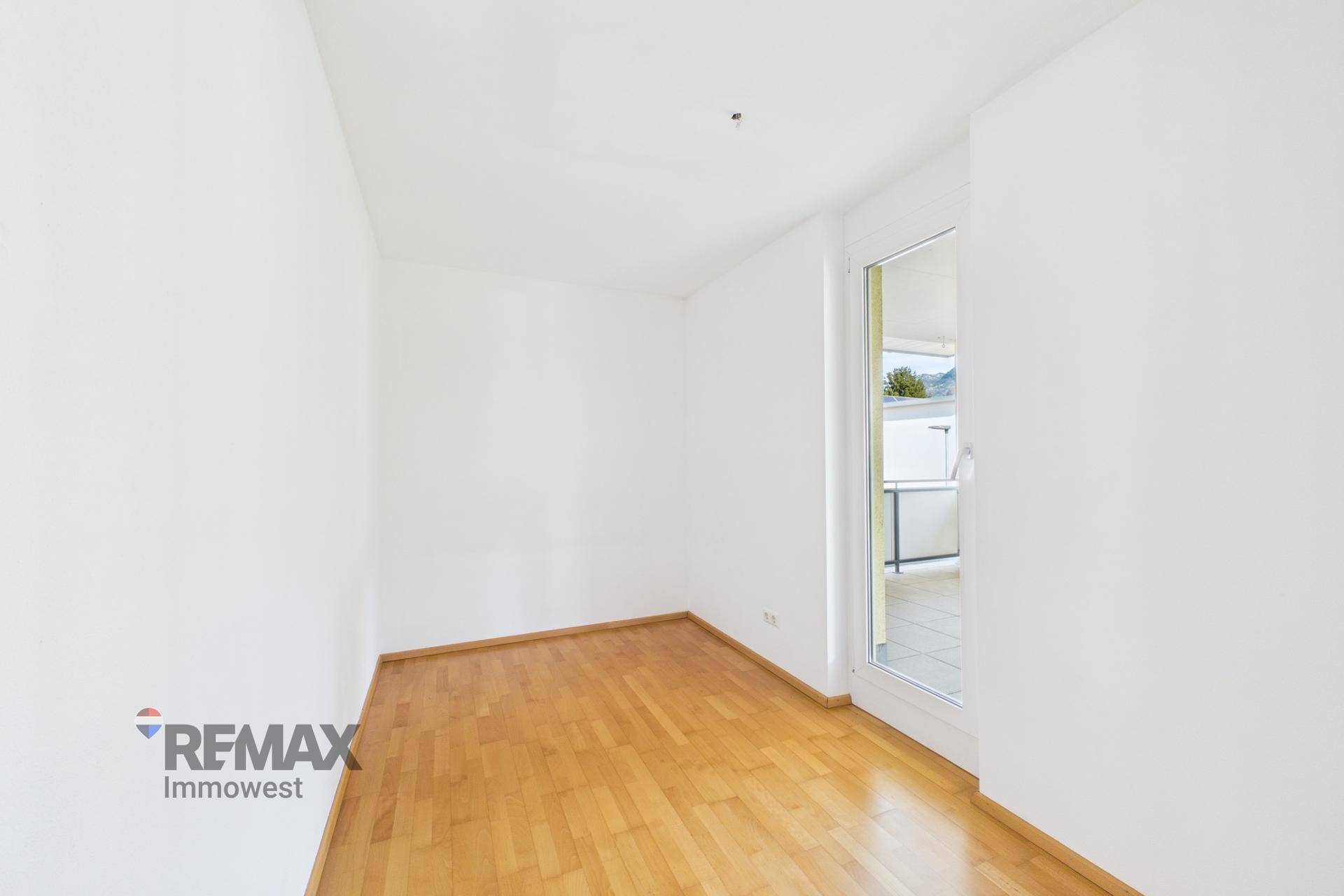 Helles Zimmer mit Parkettboden und Zugang zu einem Balkon, ideal als Schlafzimmer.