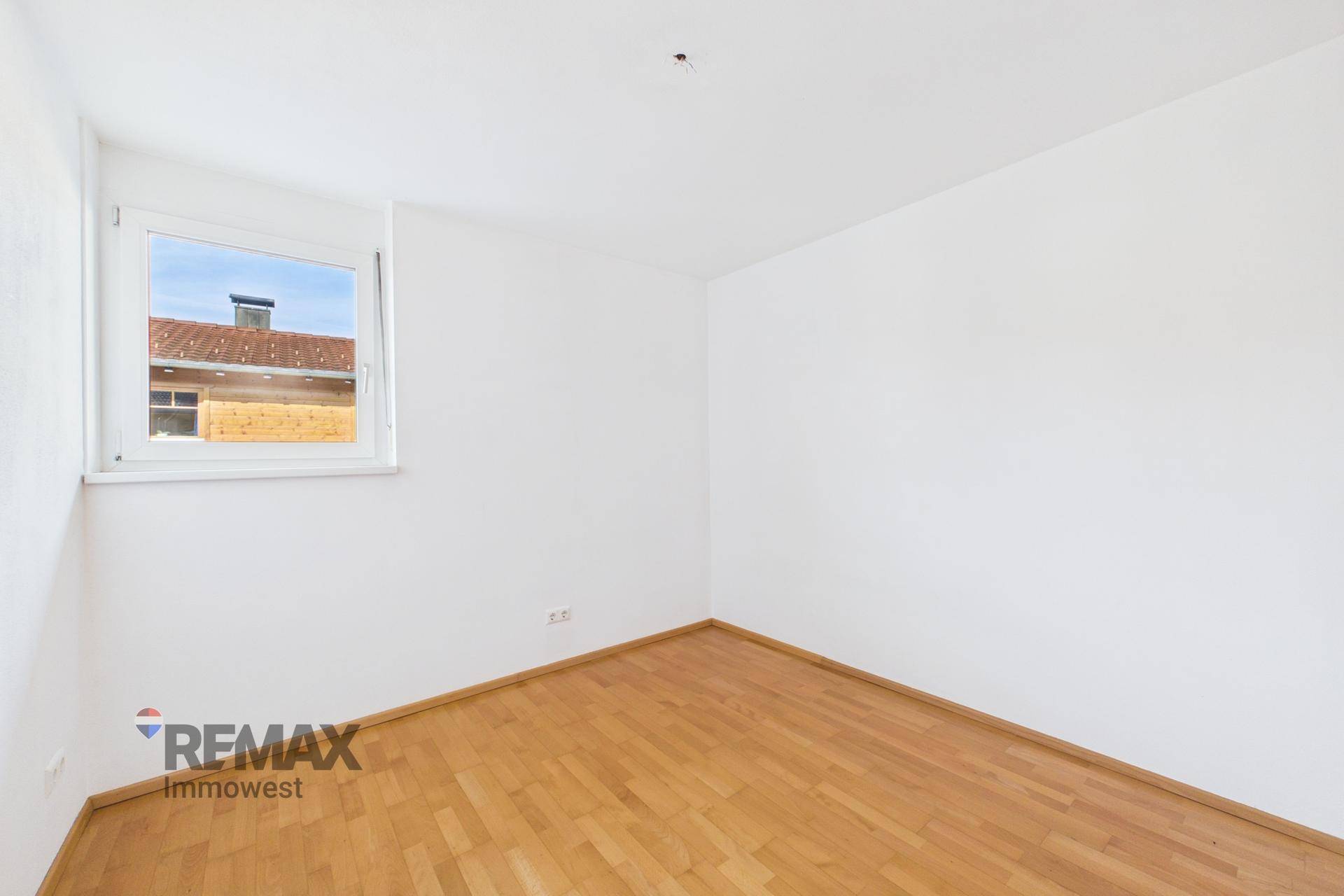 Leeres Zimmer mit Parkettboden und Fenster, das viel Tageslicht hereinlässt.