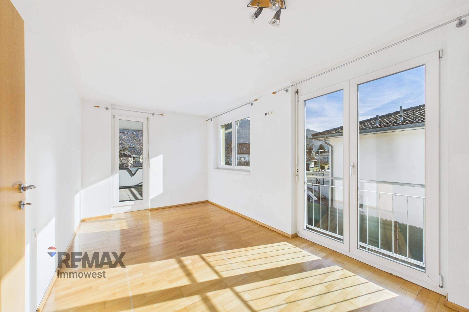 Helles Schlafzimmer mit Parkettboden und Zugang zu einem französischen Balkon.