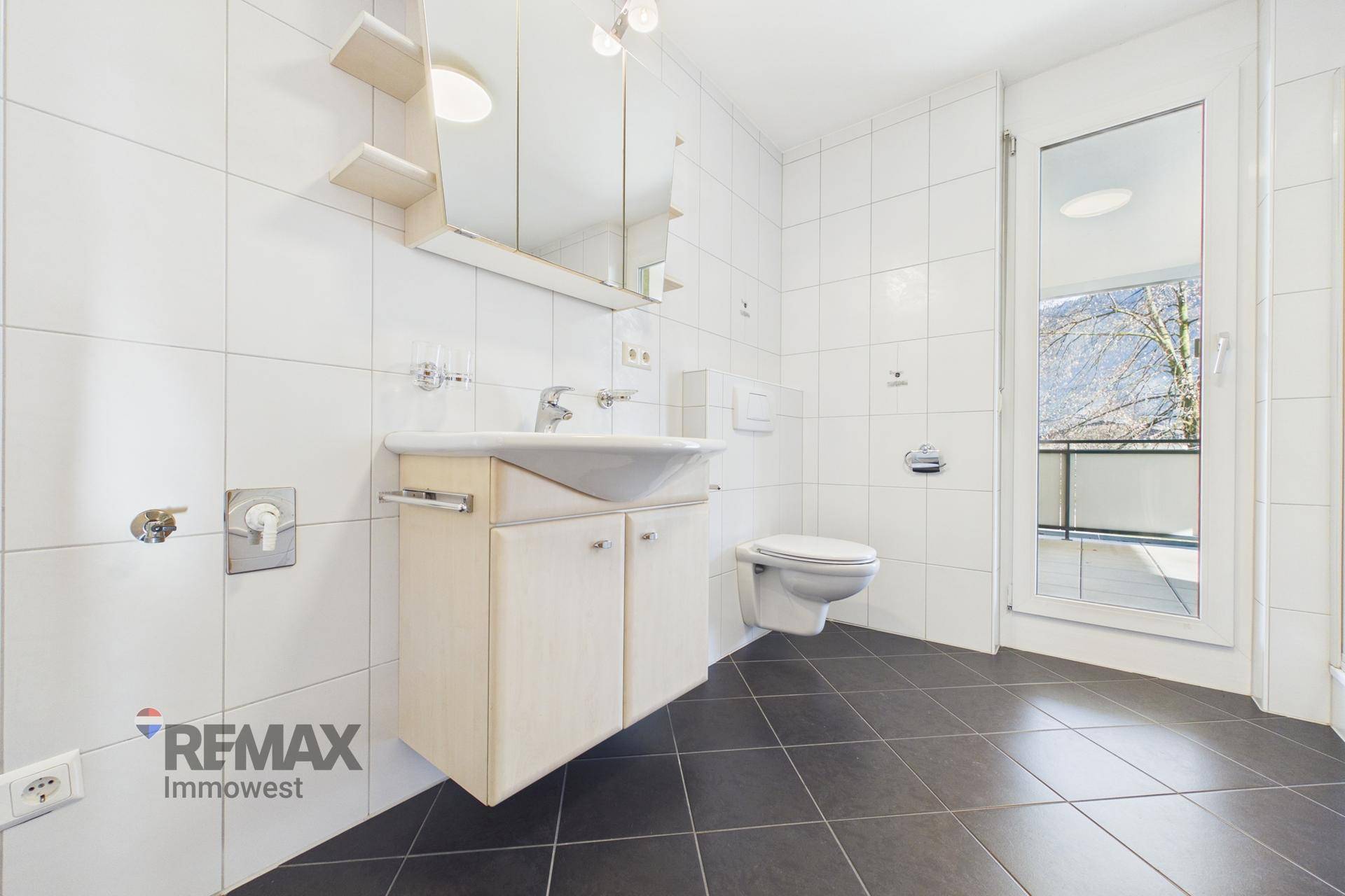 Badezimmer mit Waschbecken, Toilette, Spiegelschrank und Zugang zu einem Außenbereich.
