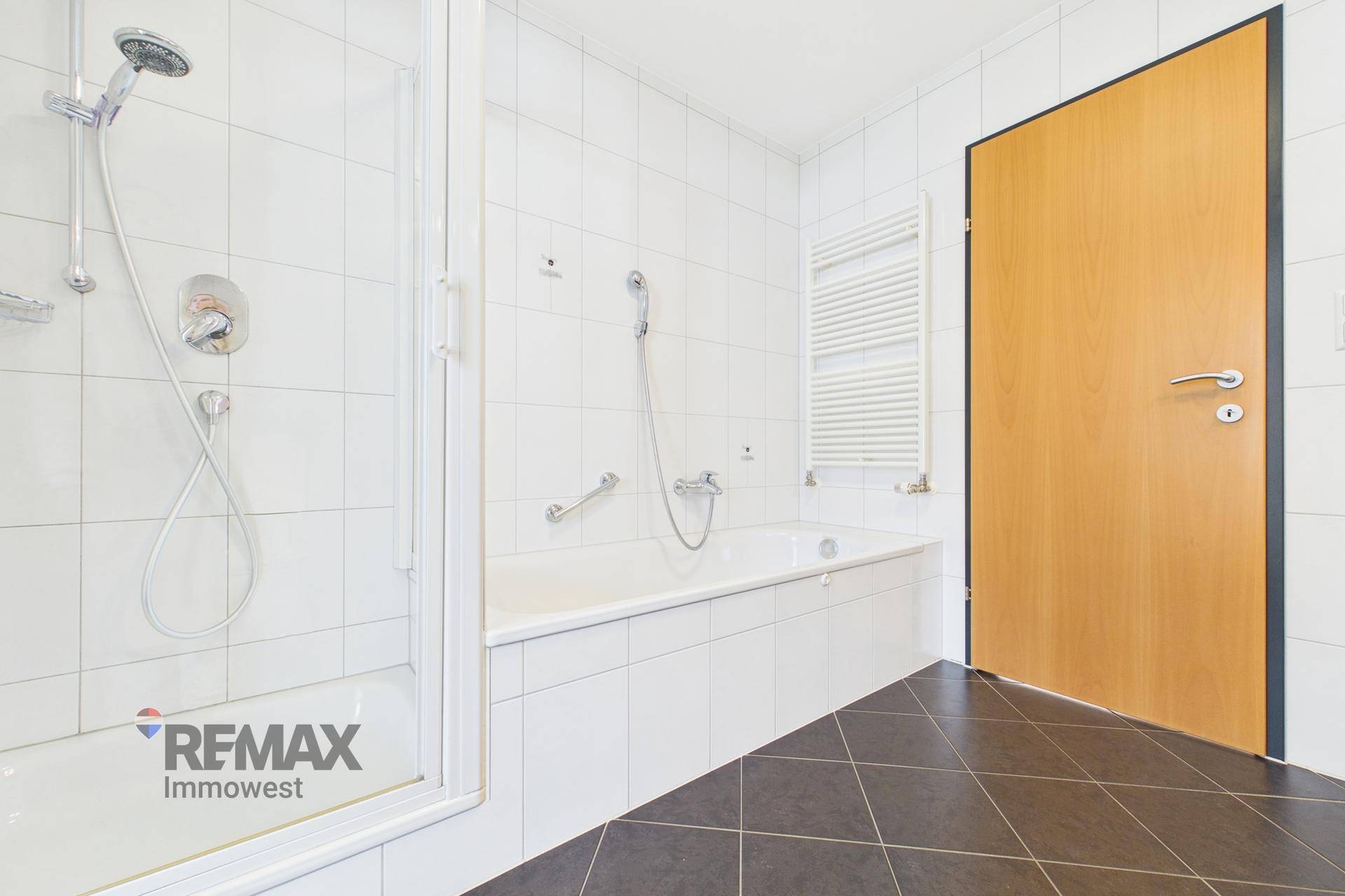 Badezimmer mit Badewanne, Duschkabine, dunklen Fliesen und beheiztem Handtuchhalter.