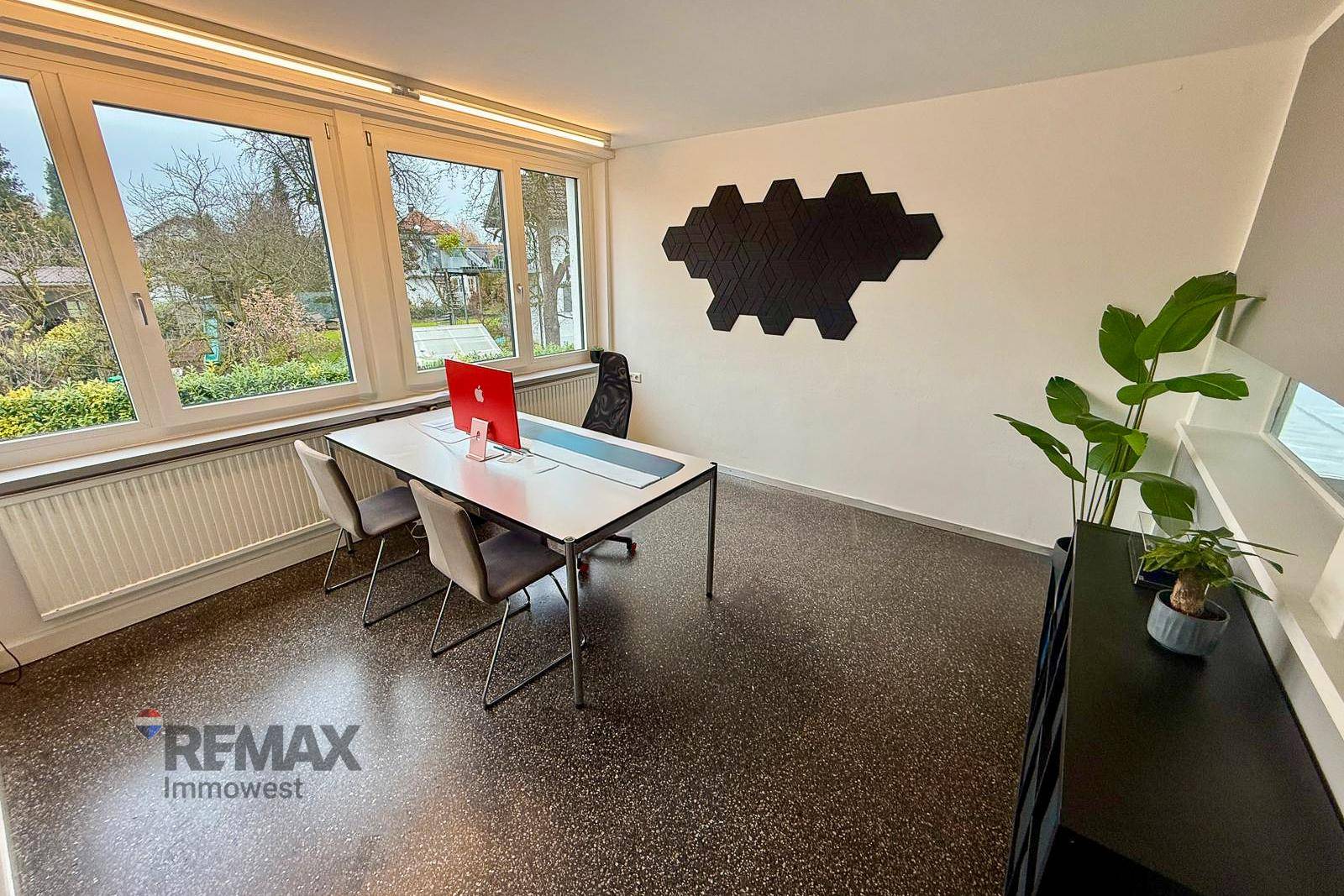 Helles Büro mit großen Fenstern, modernem Designelement an der Wand und dekorativen Pflanzen.