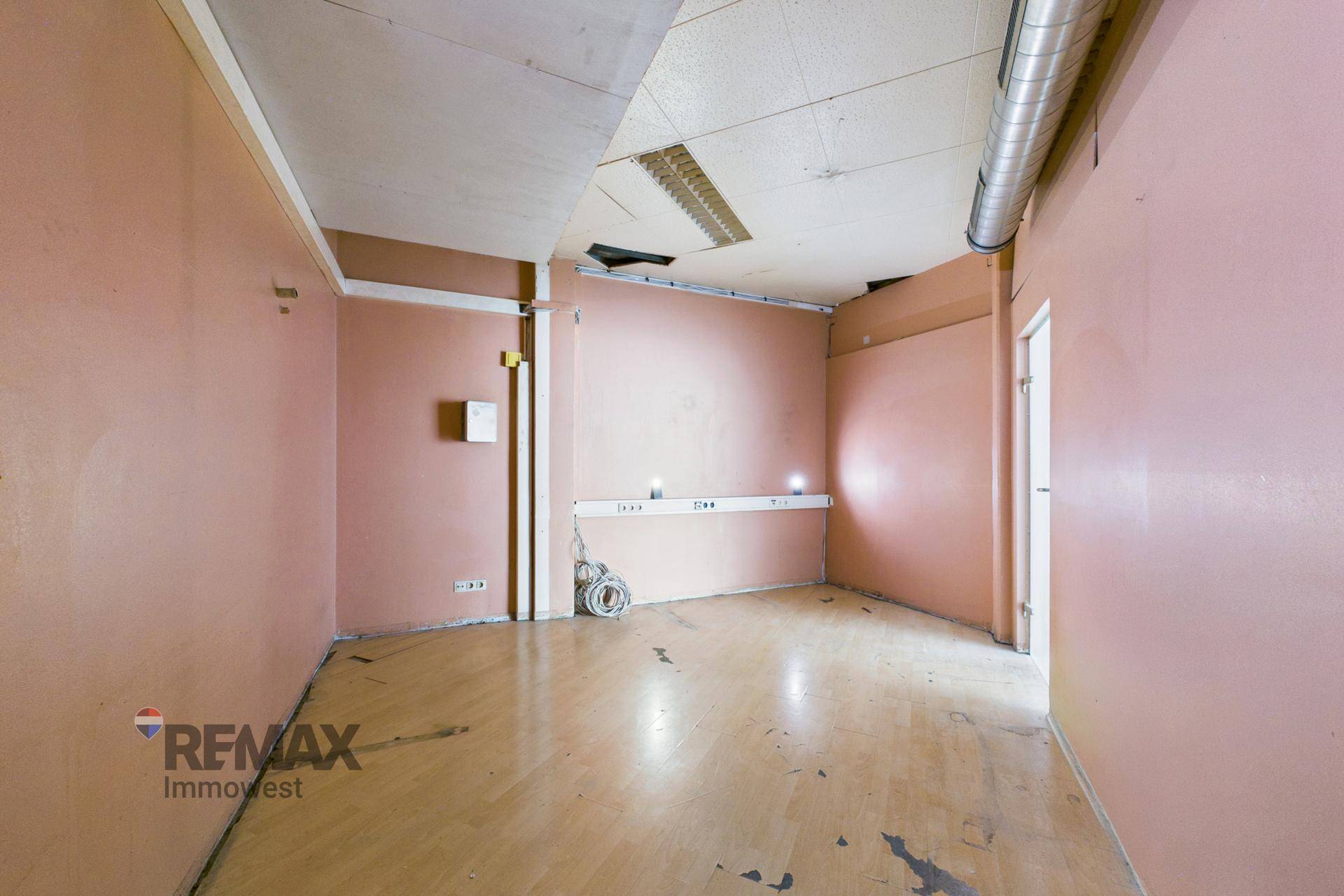 Älterer Büroraum mit rosa Wänden, Holzfußboden und einer abgehängten Decke, renovierungsbedürftig.